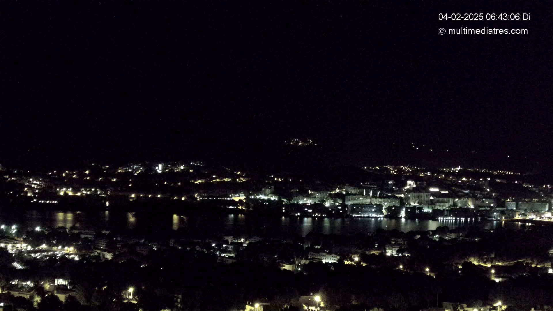 A nighttime view of a city and body of water, illuminated by numerous lights, under a clear, dark sky.