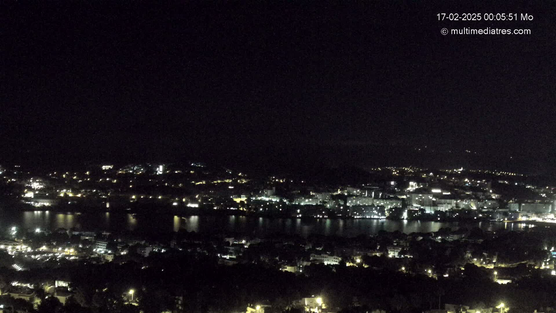 A nighttime, high-angle view of a city with a body of water reflecting the city lights.