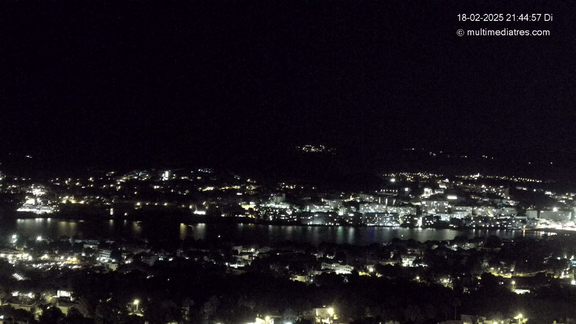 A nighttime, high-angle view of a city with a body of water reflecting the city lights.