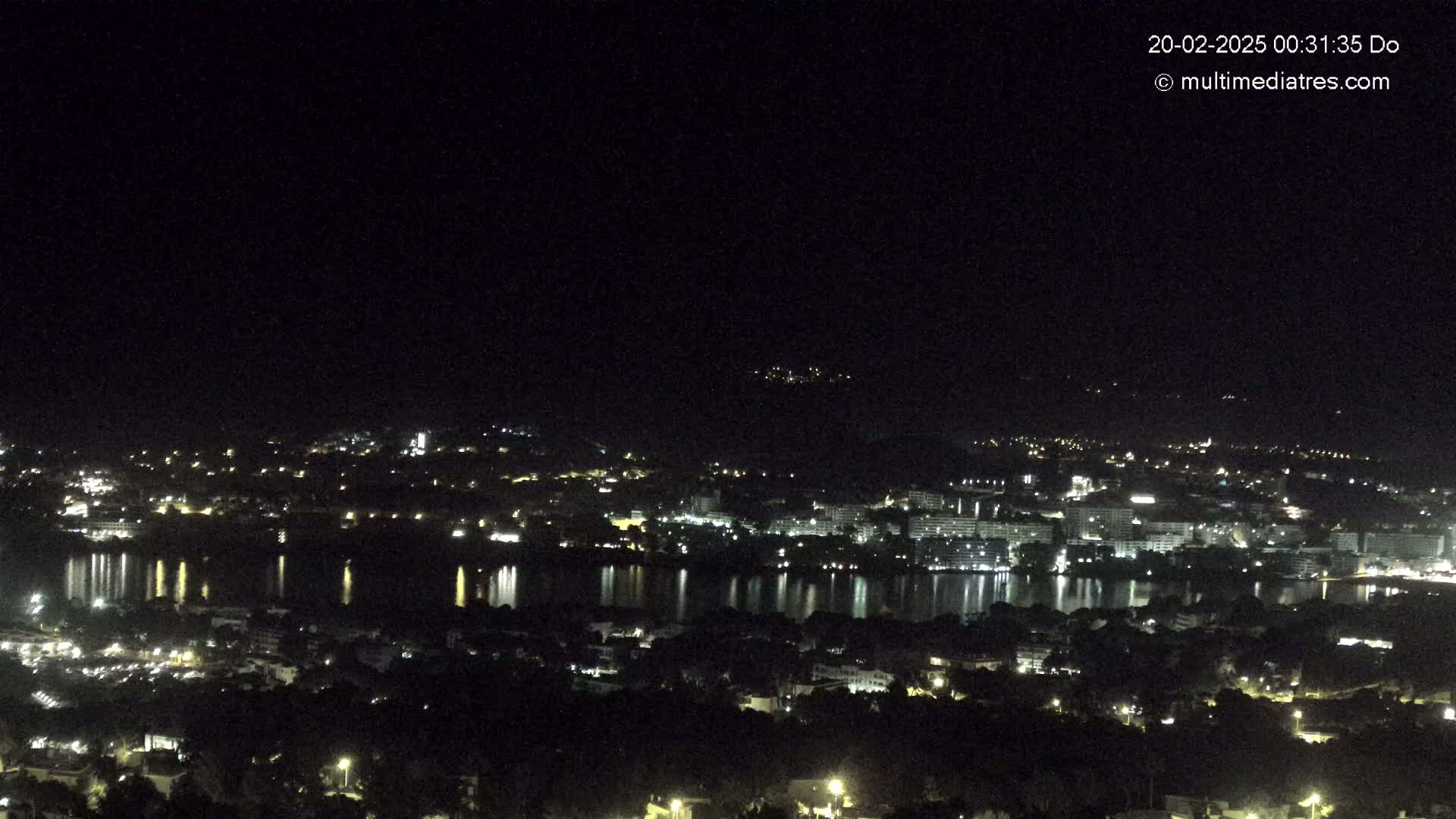 A nighttime, high-angle view of a city spread across a body of water, reflecting the city lights.