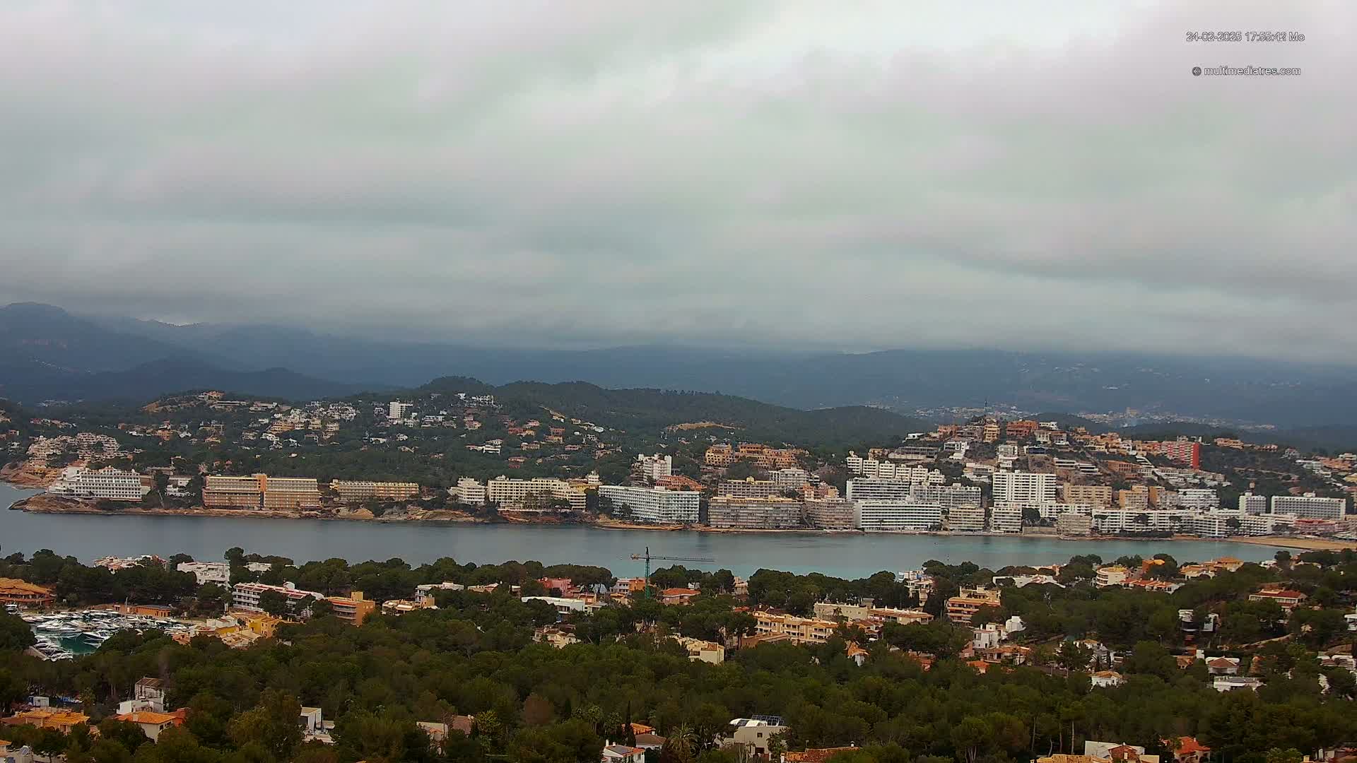 A coastal town nestled in a bay, surrounded by green hills under an overcast sky.