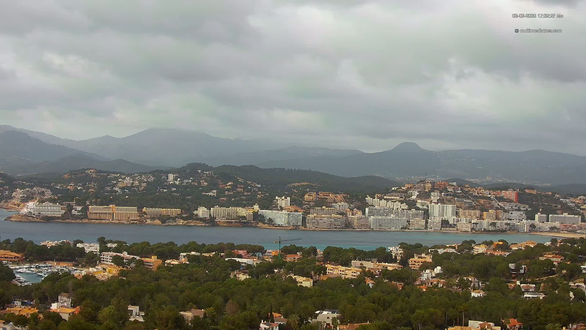 A coastal town nestled between a bay and mountains under an overcast sky.