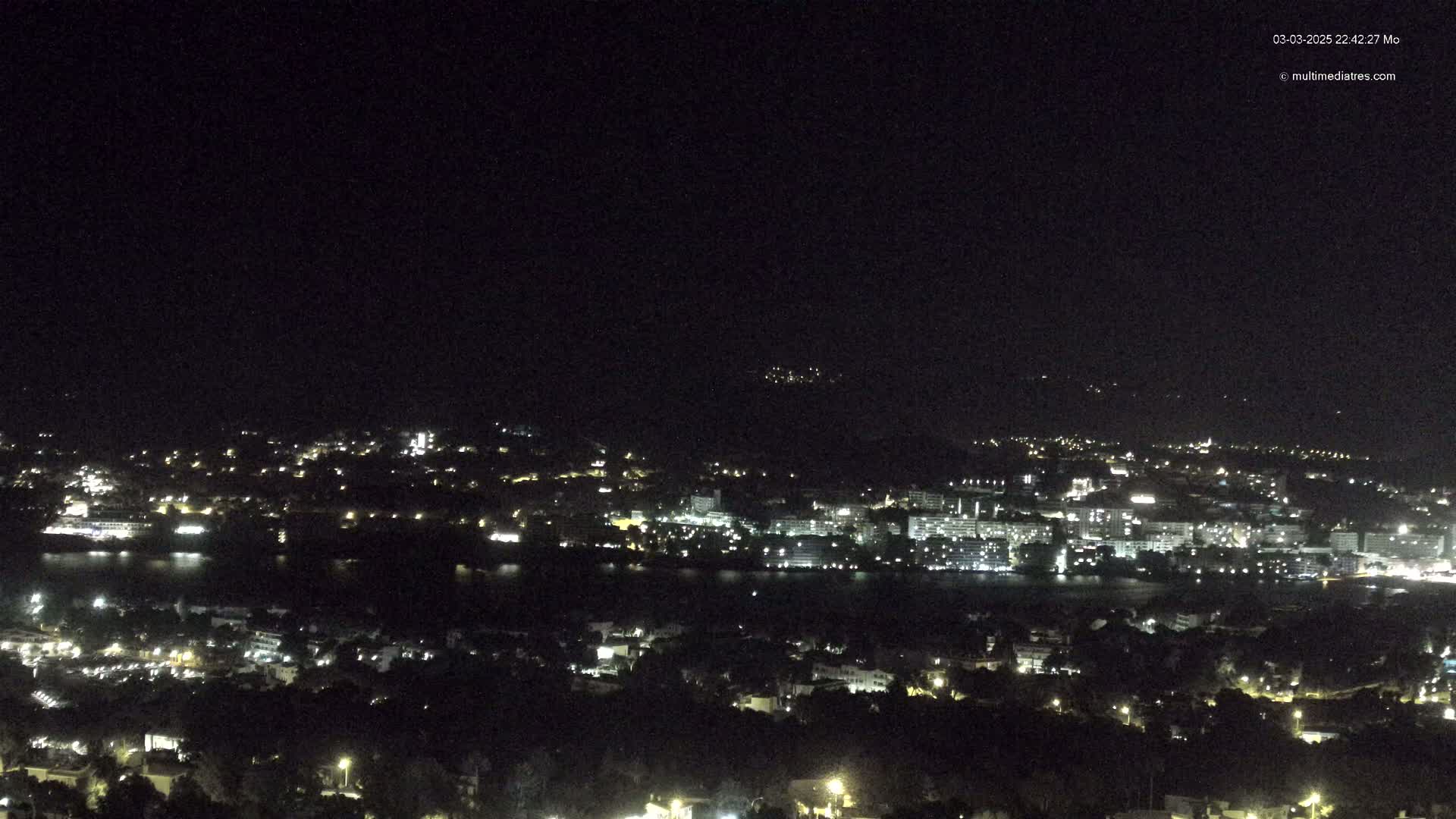 A nighttime view of a city and its waterfront, illuminated by lights, under a clear, dark sky.