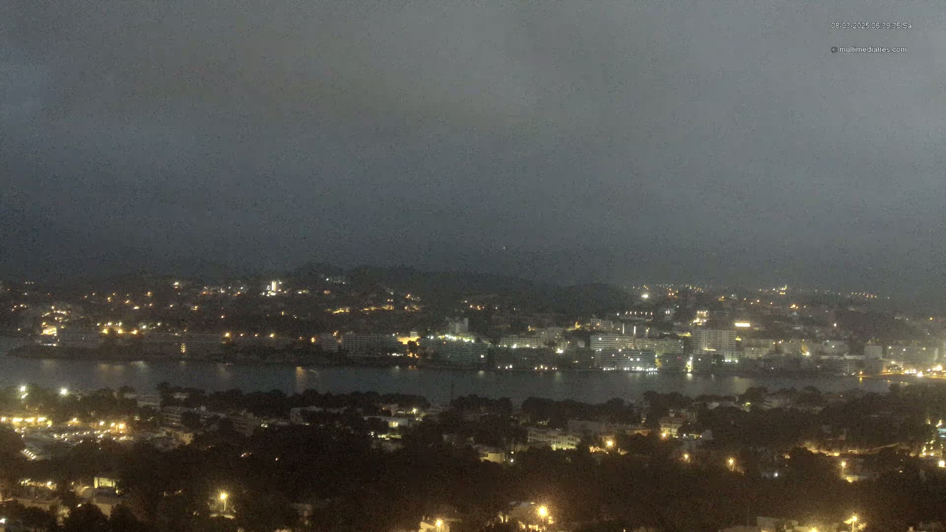 A nighttime view of a city and body of water under a dark, overcast sky.
