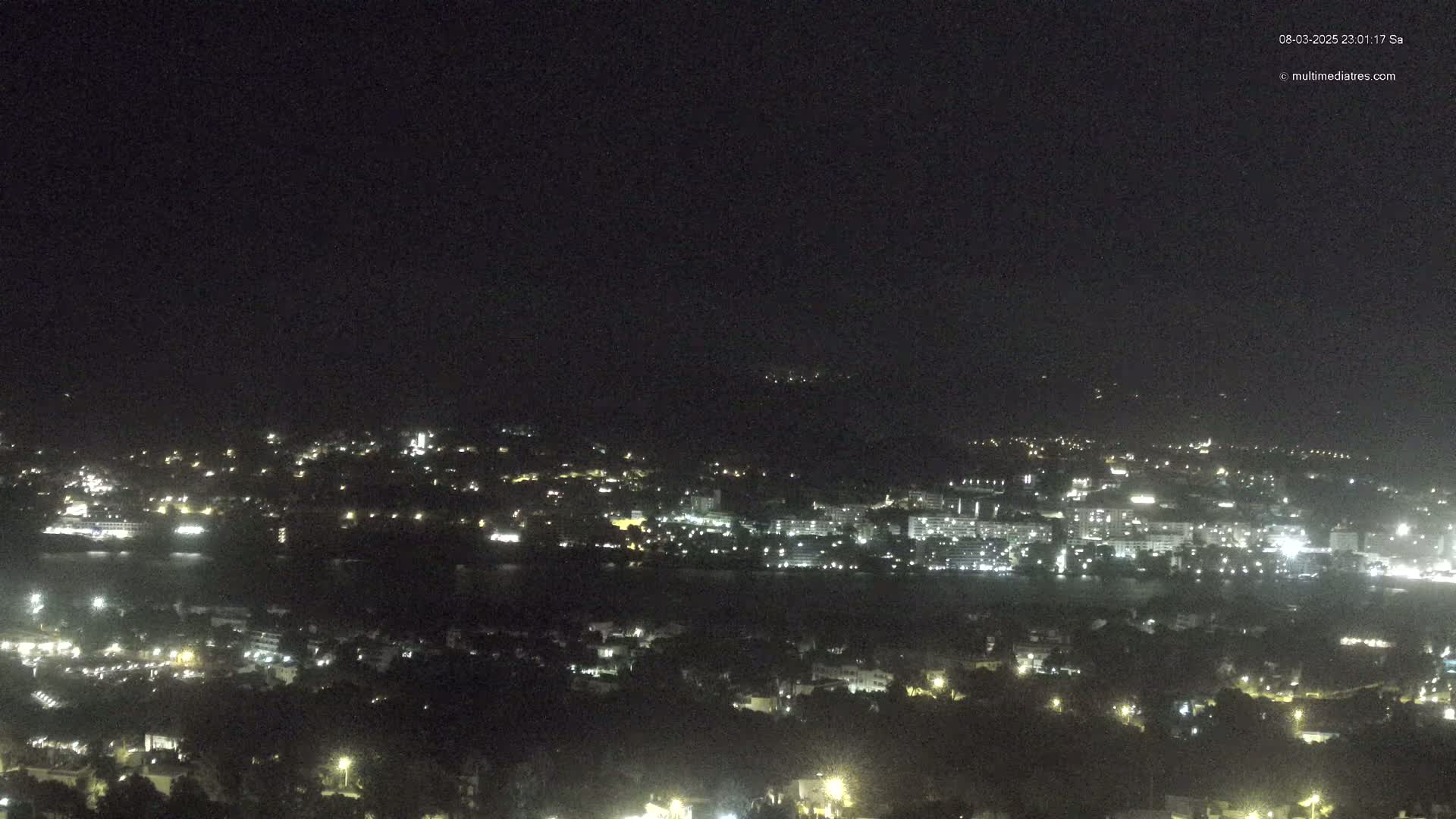 A nighttime view of a coastal town with scattered lights, under a clear, dark sky.