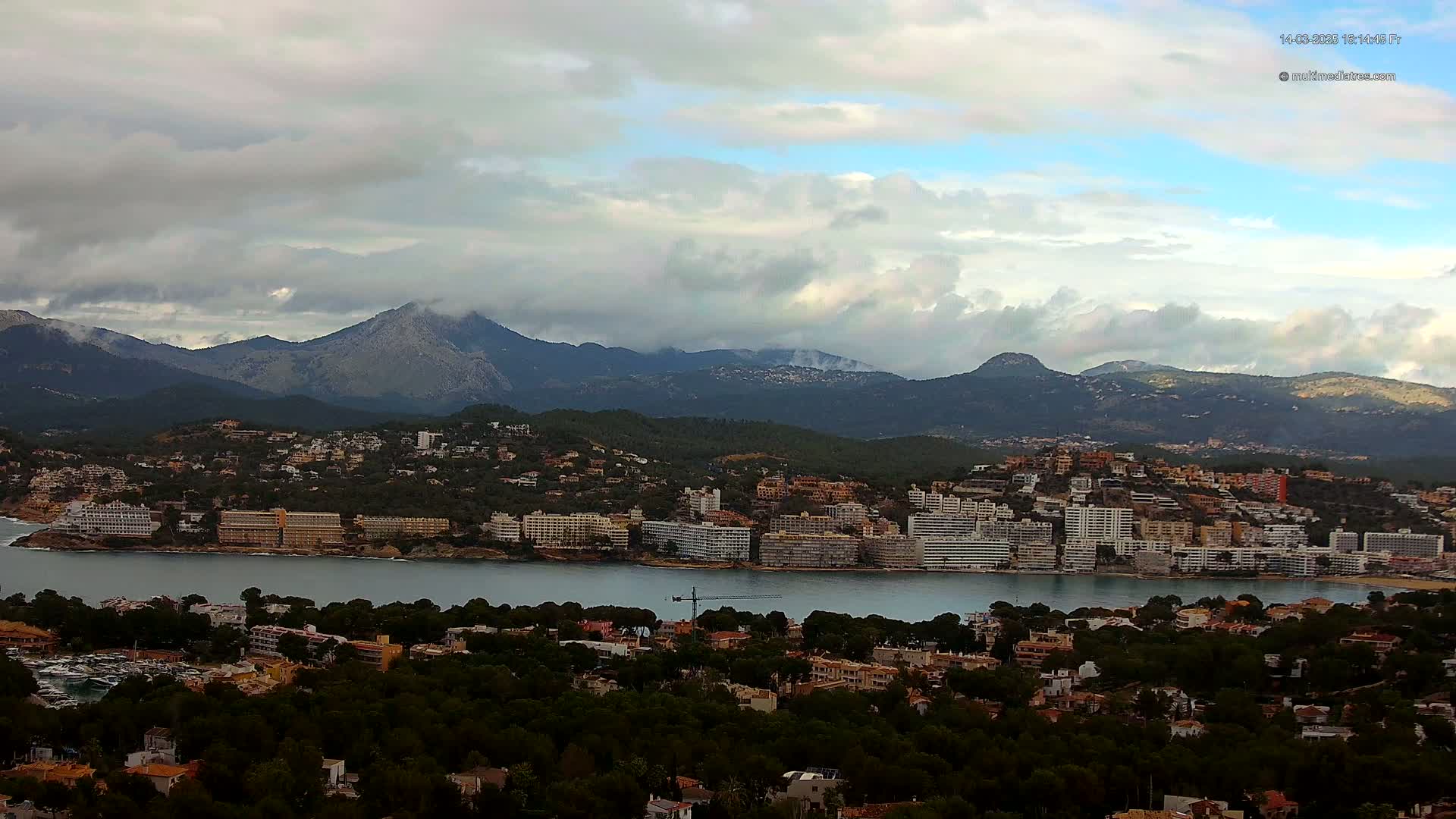 A coastal town nestled between a bay and mountains under a cloudy sky.