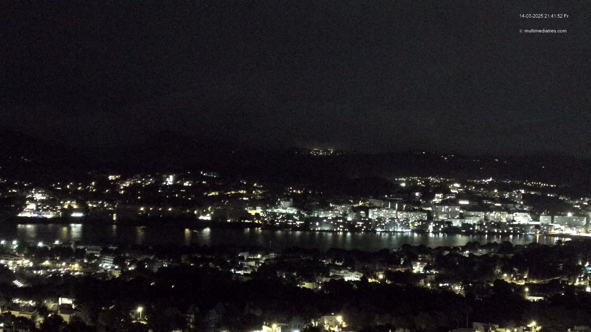 A nighttime, high-angle view of a coastal city illuminated with lights, situated on a body of dark water.