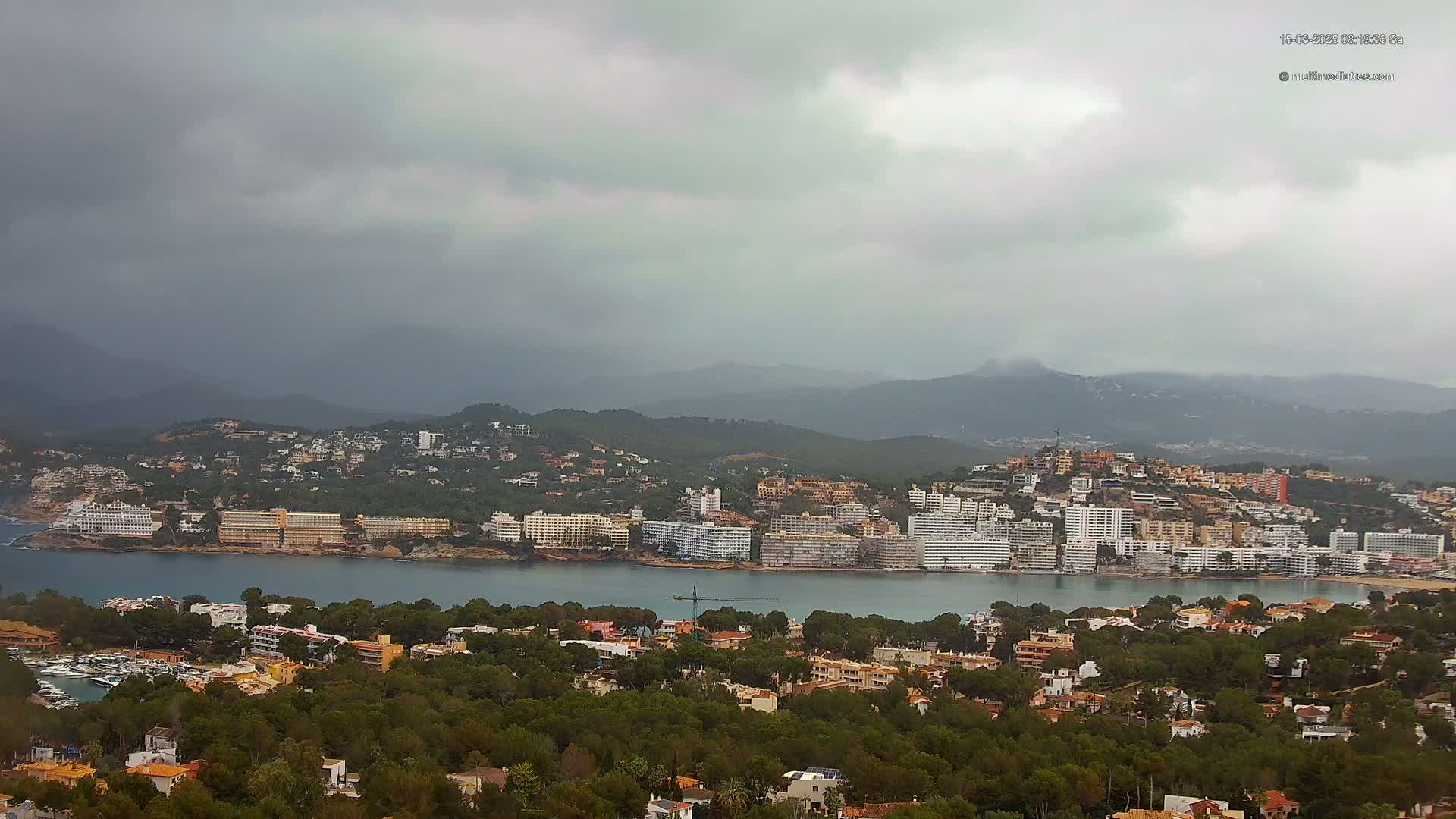 A coastal town with numerous hotels and buildings sits on a bay under a cloudy sky.