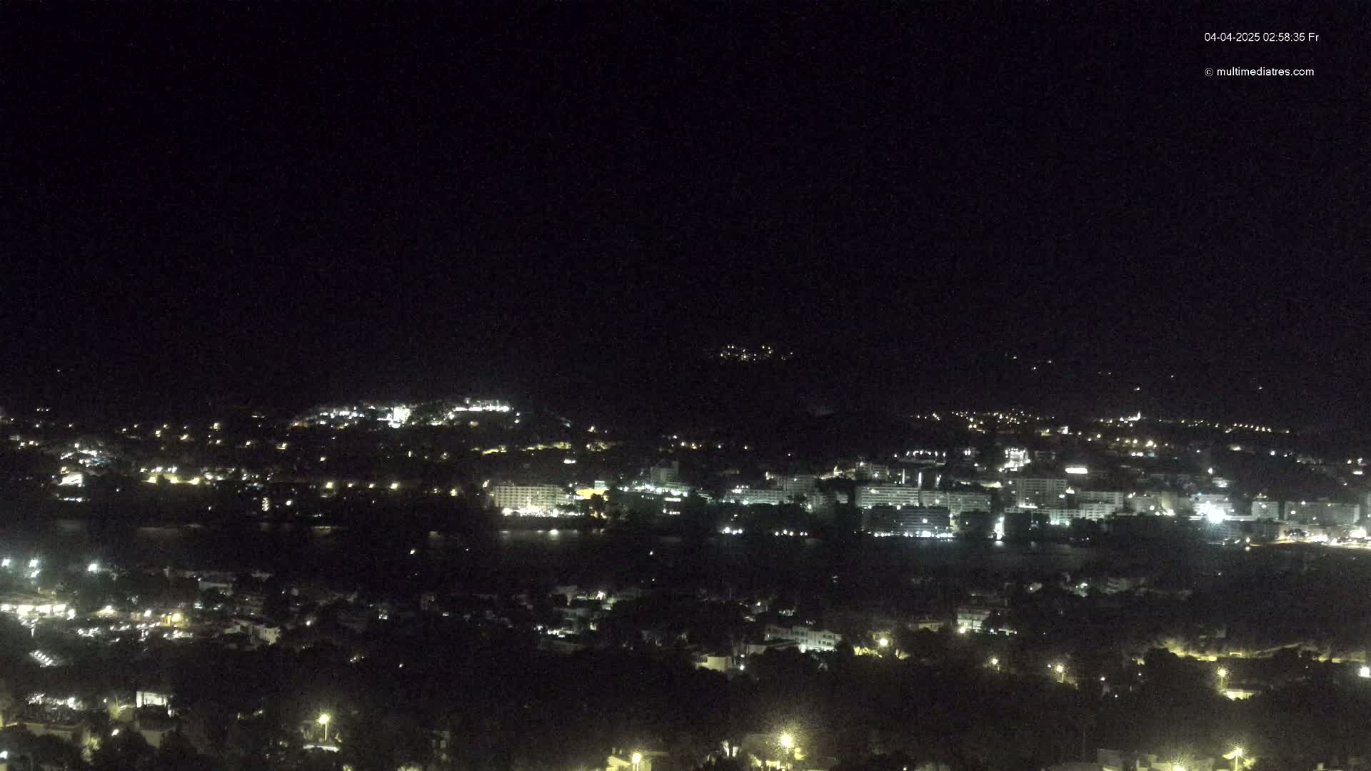 A nighttime, long-distance view of a city with many lights spread across hills and a body of water.