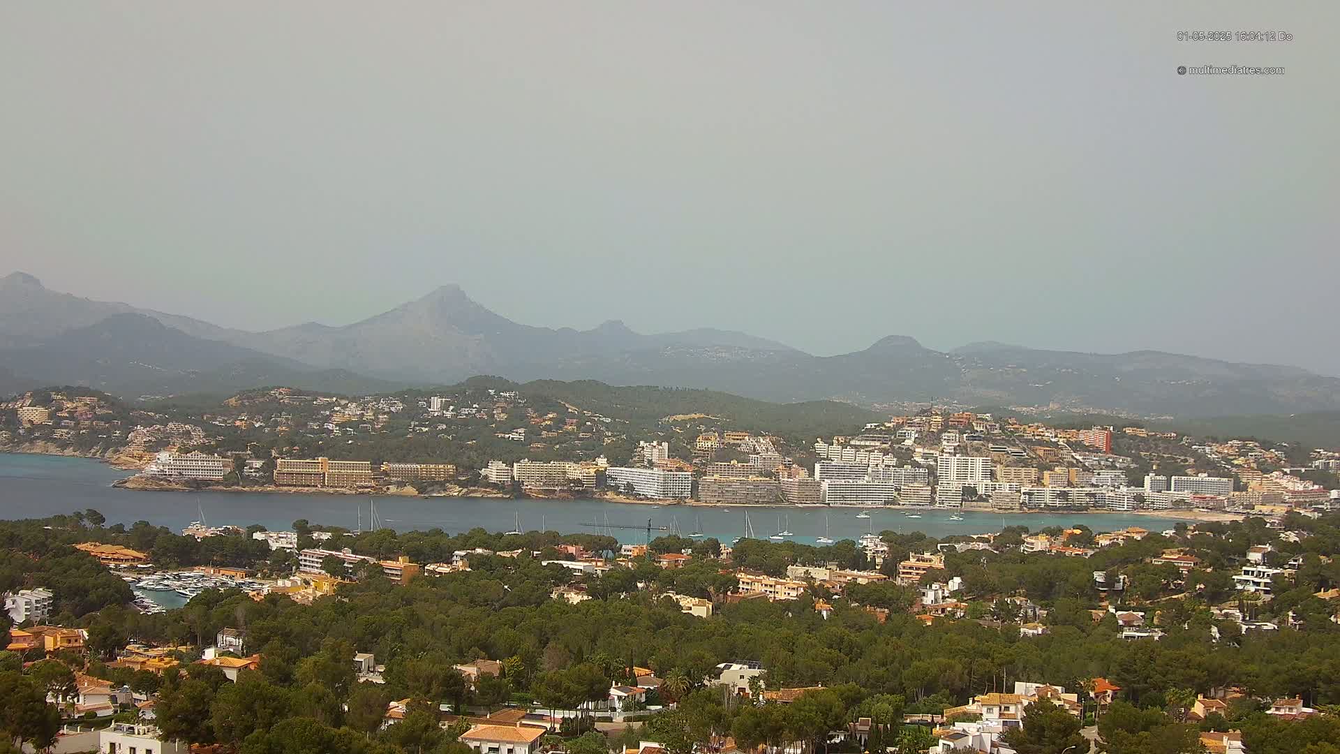 A hazy coastal town nestled between a calm bay and a mountain range.
