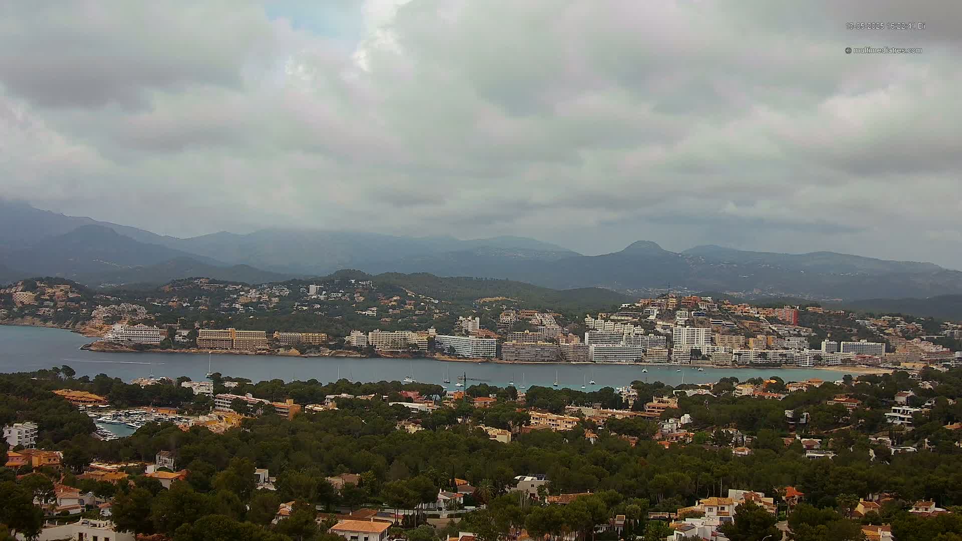 A coastal town nestled between a bay and mountains under an overcast sky.