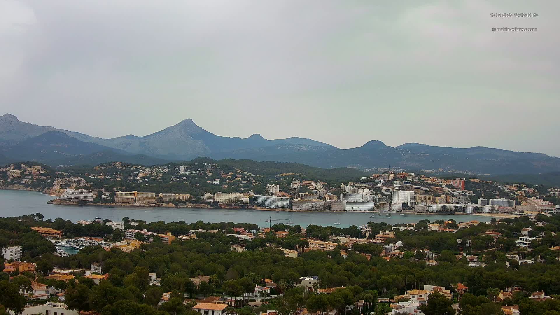 A coastal town nestled against a mountain range under an overcast sky.