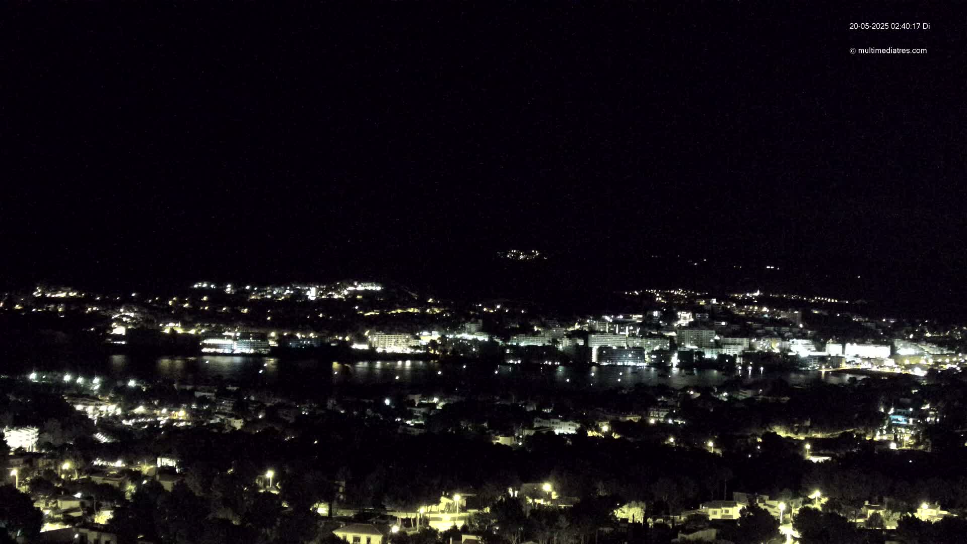 A nighttime view of a coastal town with many lights, under a clear, dark sky.