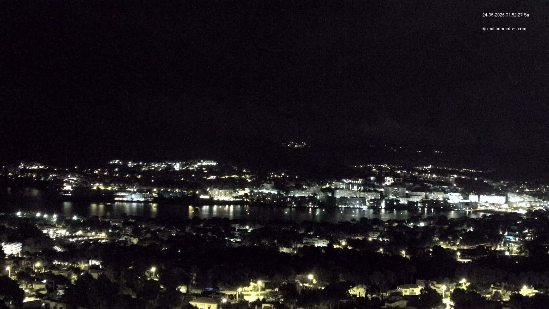 A nighttime view of a city and body of water, illuminated by lights, with a dark sky.