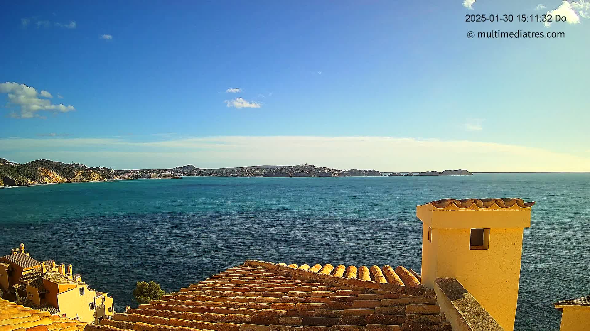 A clear, sunny day overlooks a calm ocean with a distant coastline, viewed from a tiled roof with a yellow chimney.