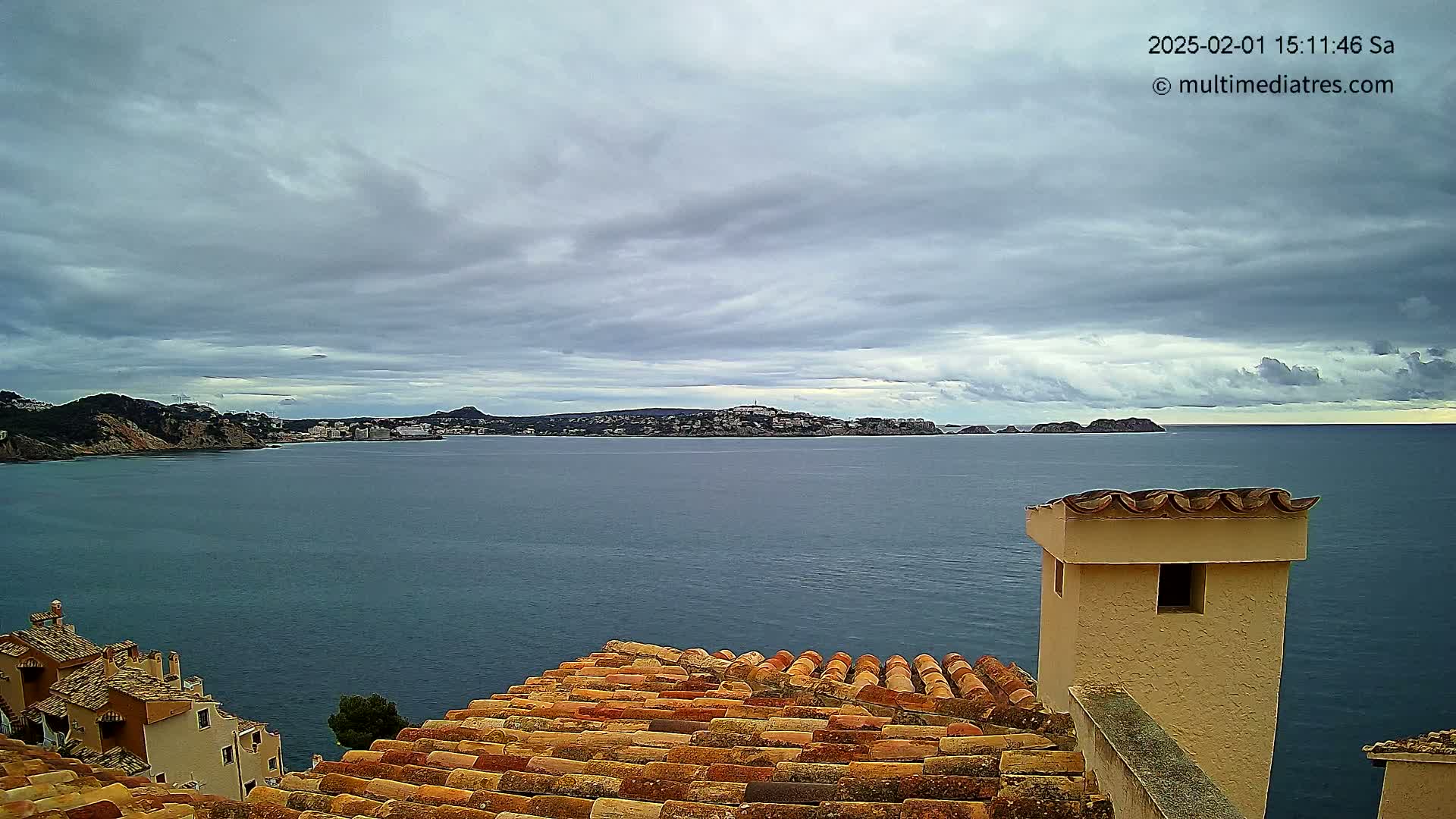 A coastal town with terracotta rooftops overlooks a calm sea under a cloudy sky.