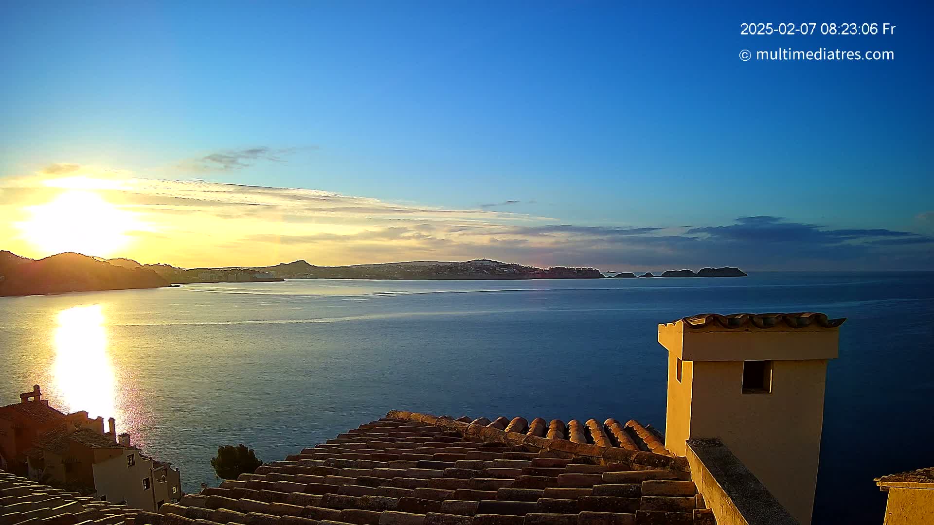 A sunrise over a calm sea, seen from a rooftop with terracotta tiles and a small, tan chimney.