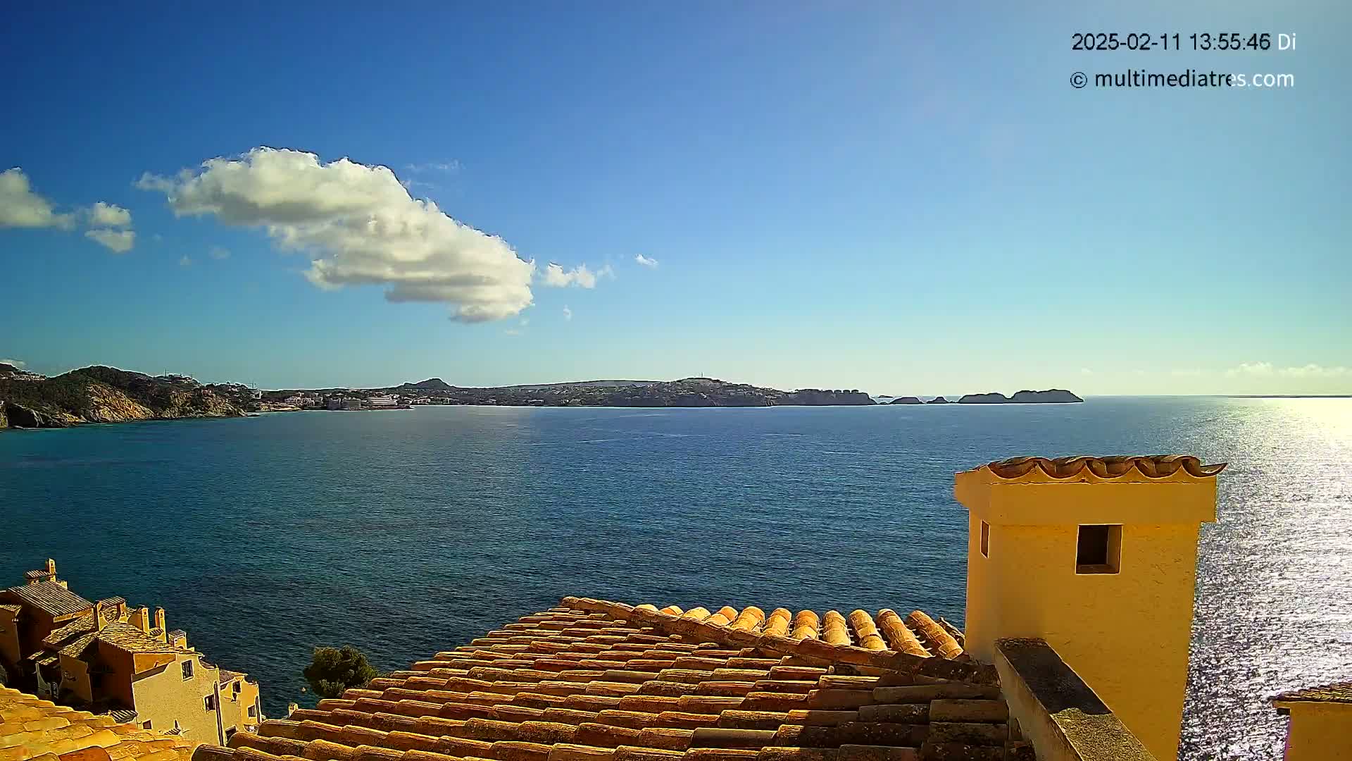 A view from a tiled rooftop shows a calm, blue sea under a mostly clear sky with a single puffy cloud, and distant landmasses.