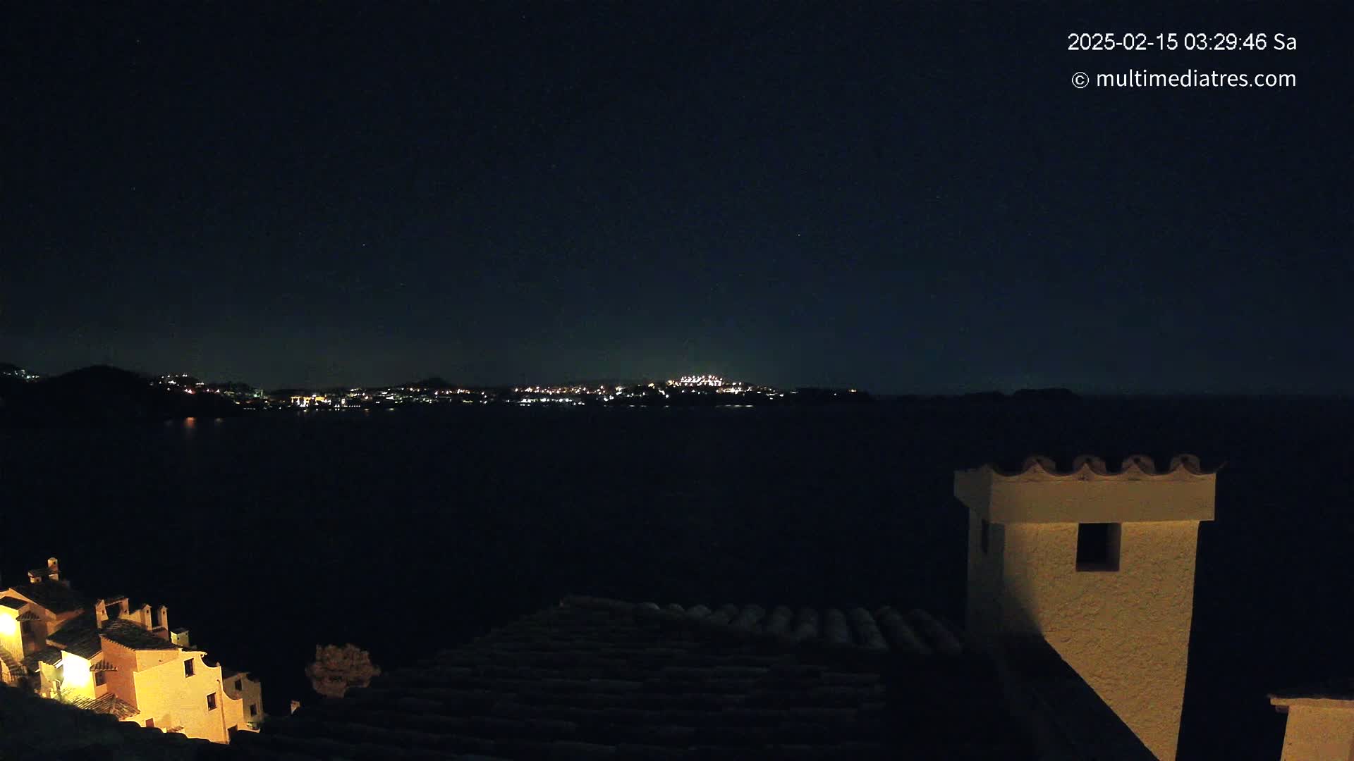 A nighttime view of a city across a dark body of water, seen from a high vantage point overlooking buildings with a clear, starry sky.