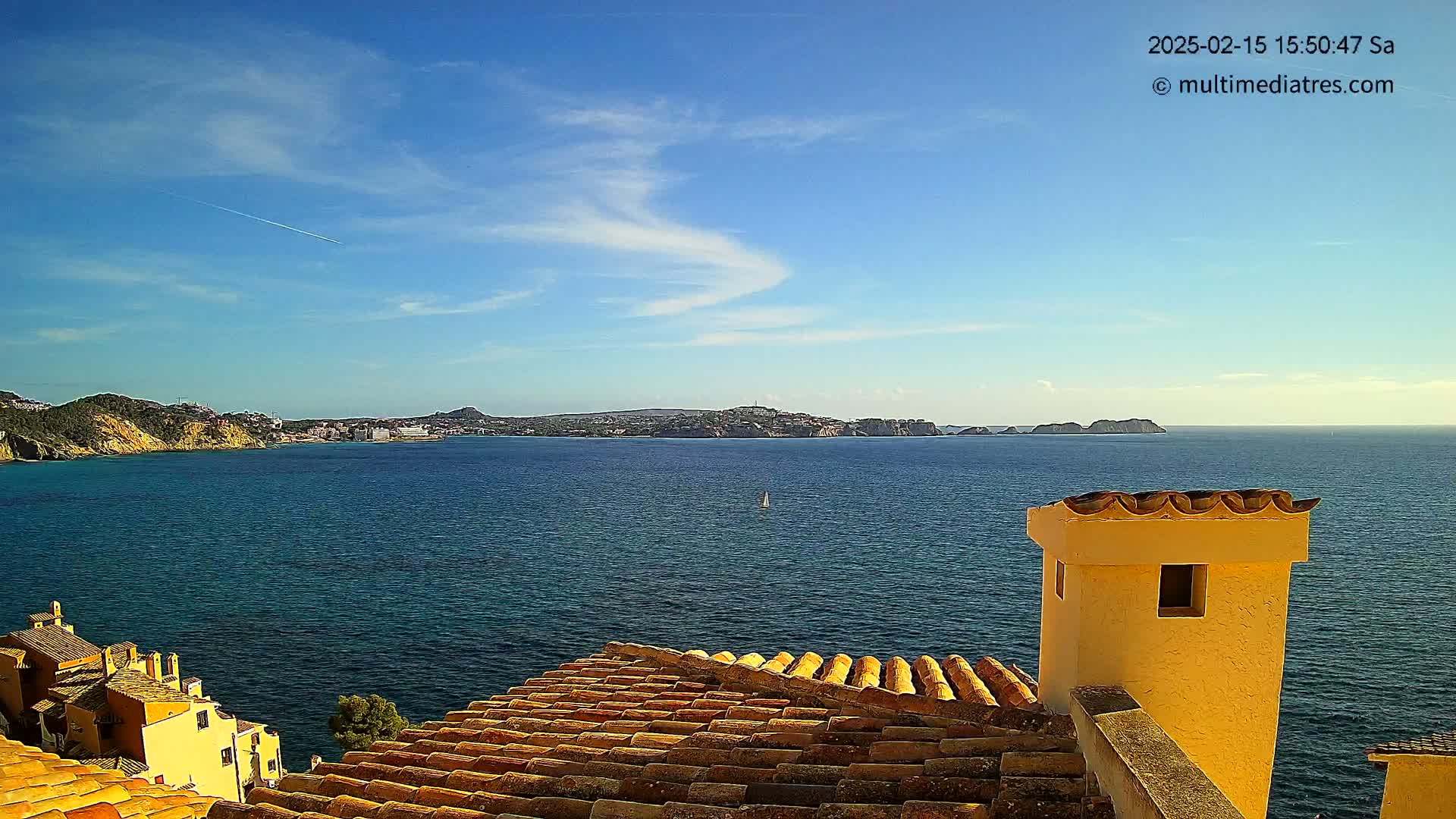 A view from a terracotta roof shows a calm, blue sea under a mostly sunny sky with a few wispy clouds, and a distant coastline with buildings.