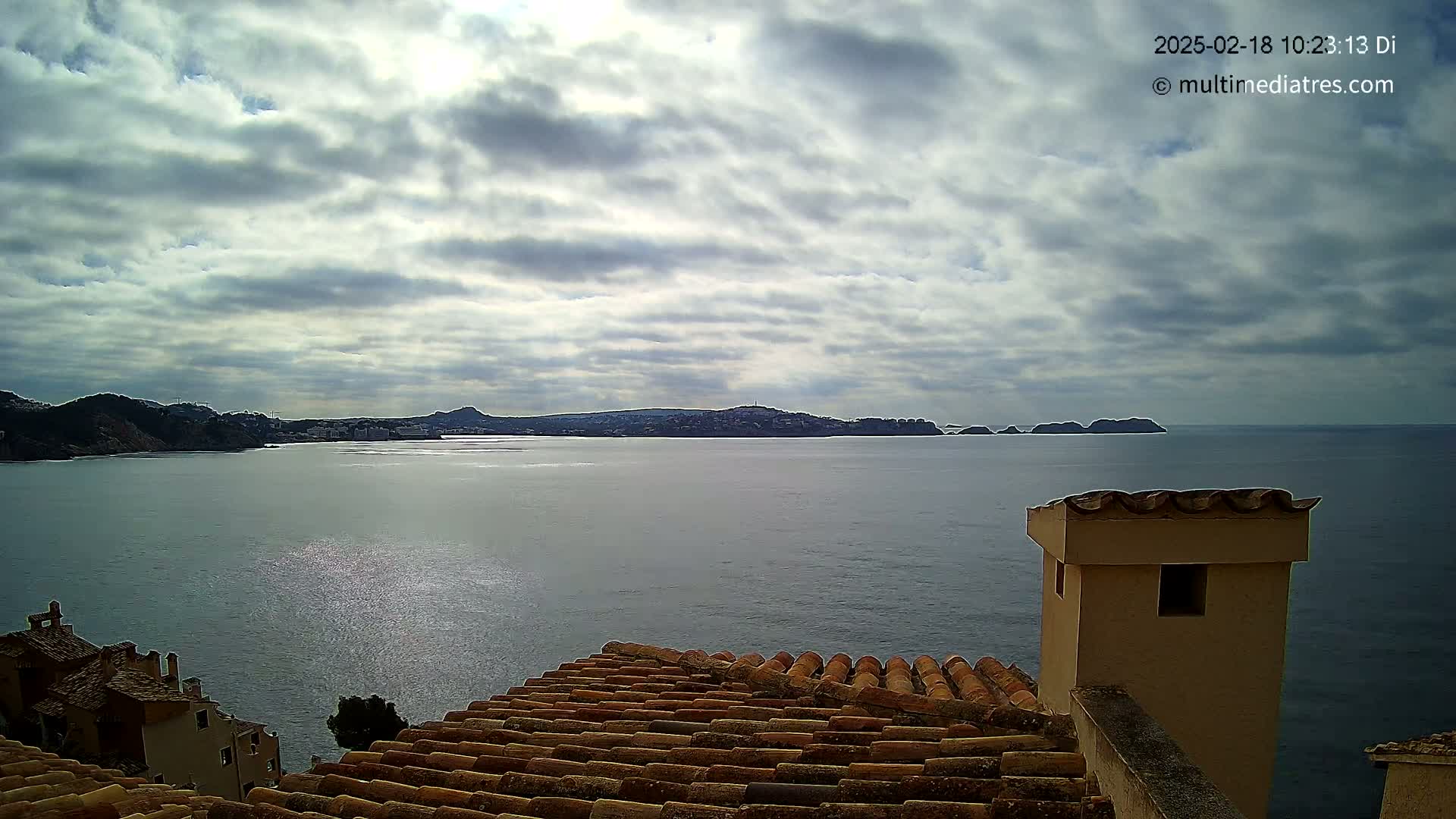 A view from a tiled roof shows a calm sea with distant hills and a cloudy sky.