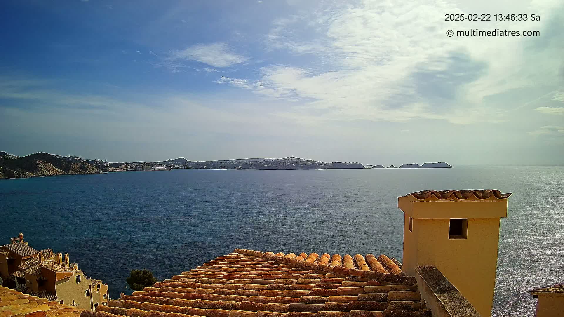 A view from a terracotta roof shows a calm blue sea with a distant island under a partly cloudy, sunny sky.
