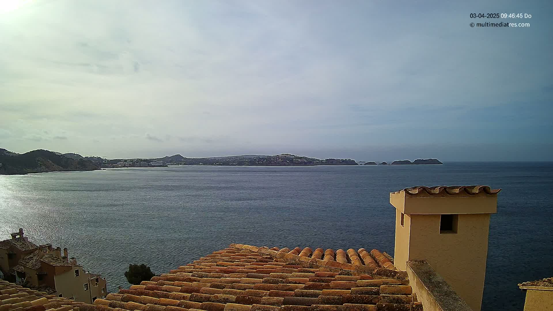 A view from a tiled roof shows a calm ocean with a distant coastline under a partly cloudy sky.