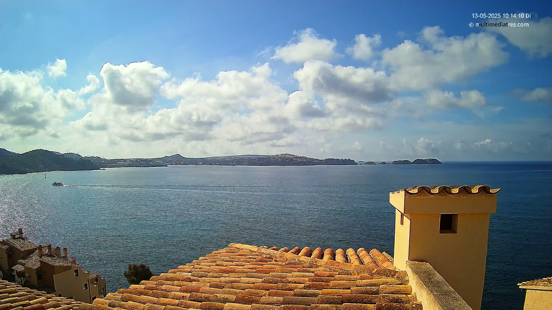 A partly cloudy sky overlooks a calm ocean with a distant coastline, viewed from a terracotta roof with a tan chimney.