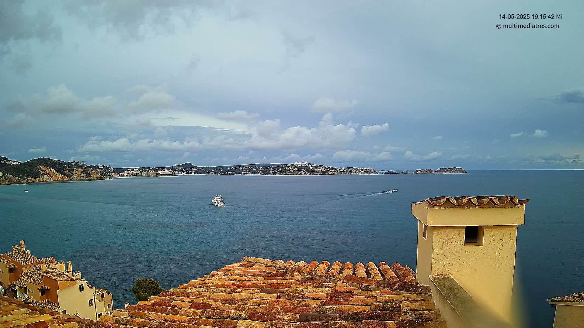 A partly cloudy sky overlooks a calm sea with a boat and distant shoreline, viewed from a tiled rooftop with a chimney.