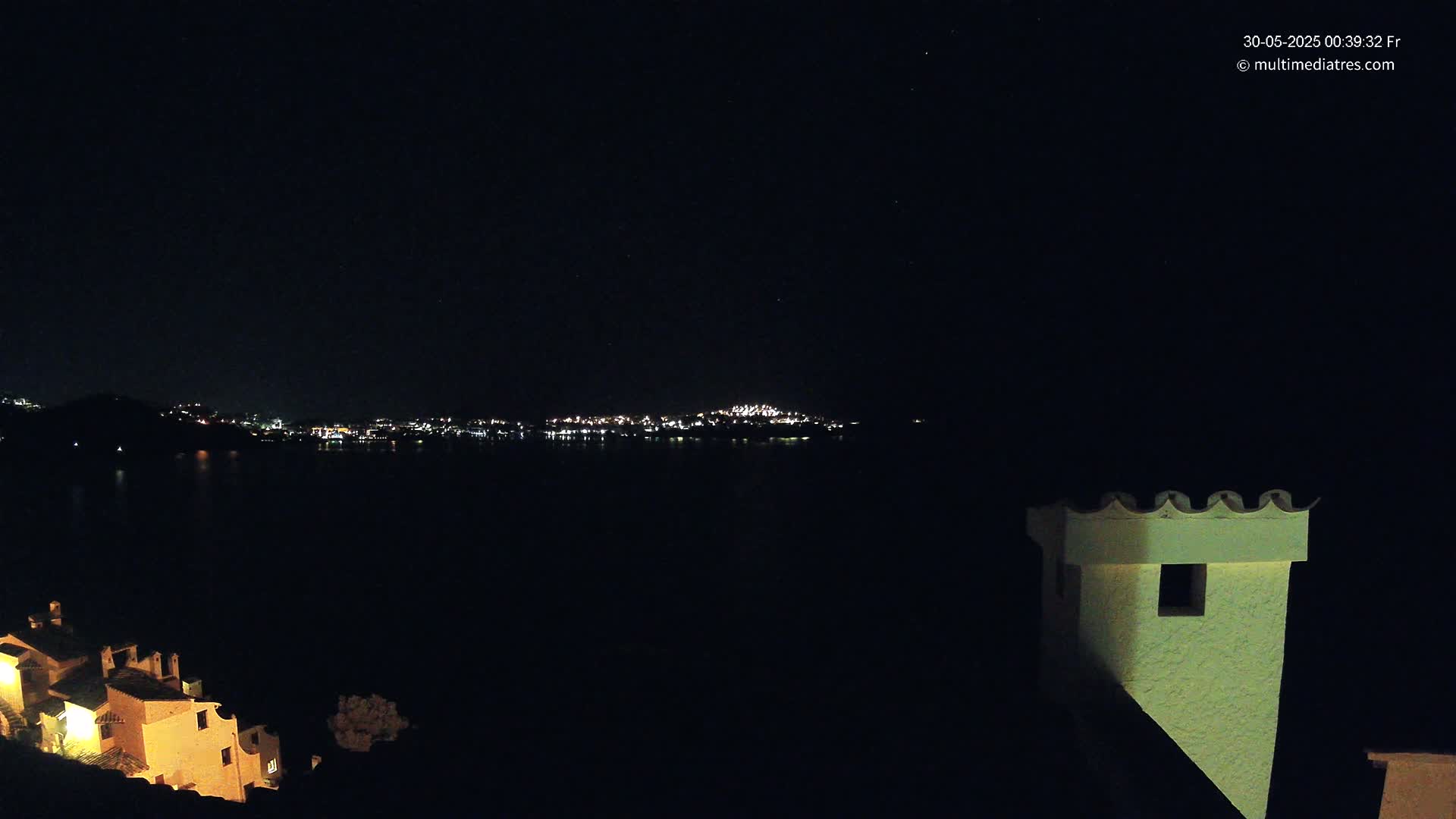 A nighttime view of a city across a dark body of water, with illuminated buildings in the foreground and a clear, starry sky.