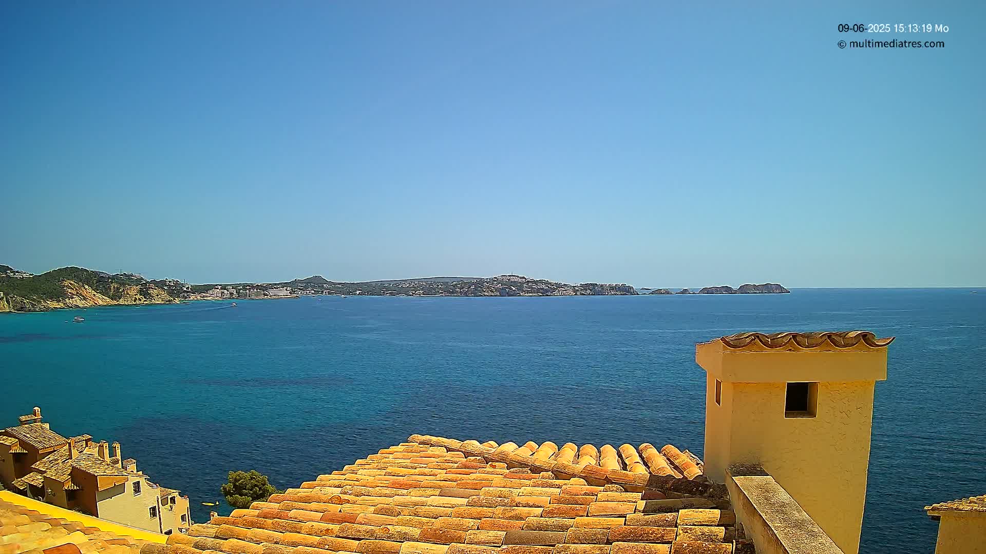 A terracotta roof overlooks a clear blue sea and distant coastline under a bright sunny sky.