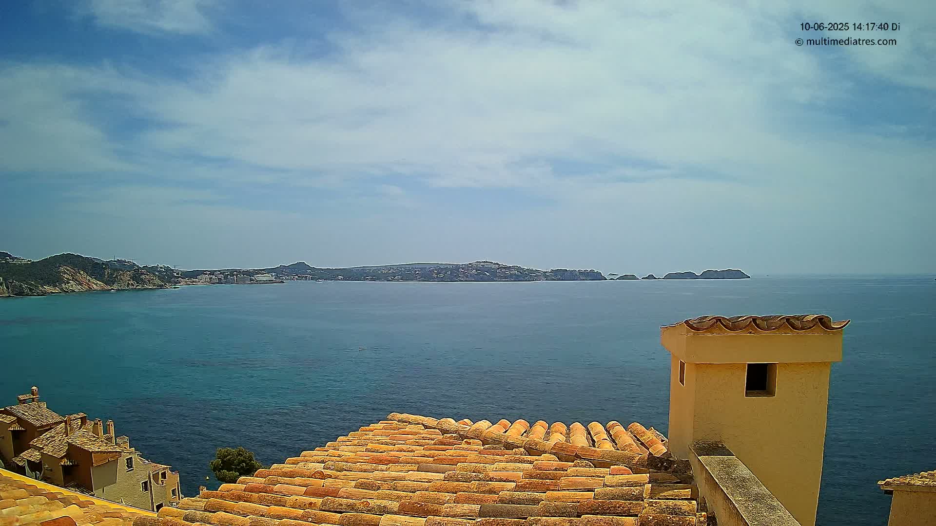 A terracotta roof overlooks a calm, blue sea with a distant coastline under a mostly sunny sky.