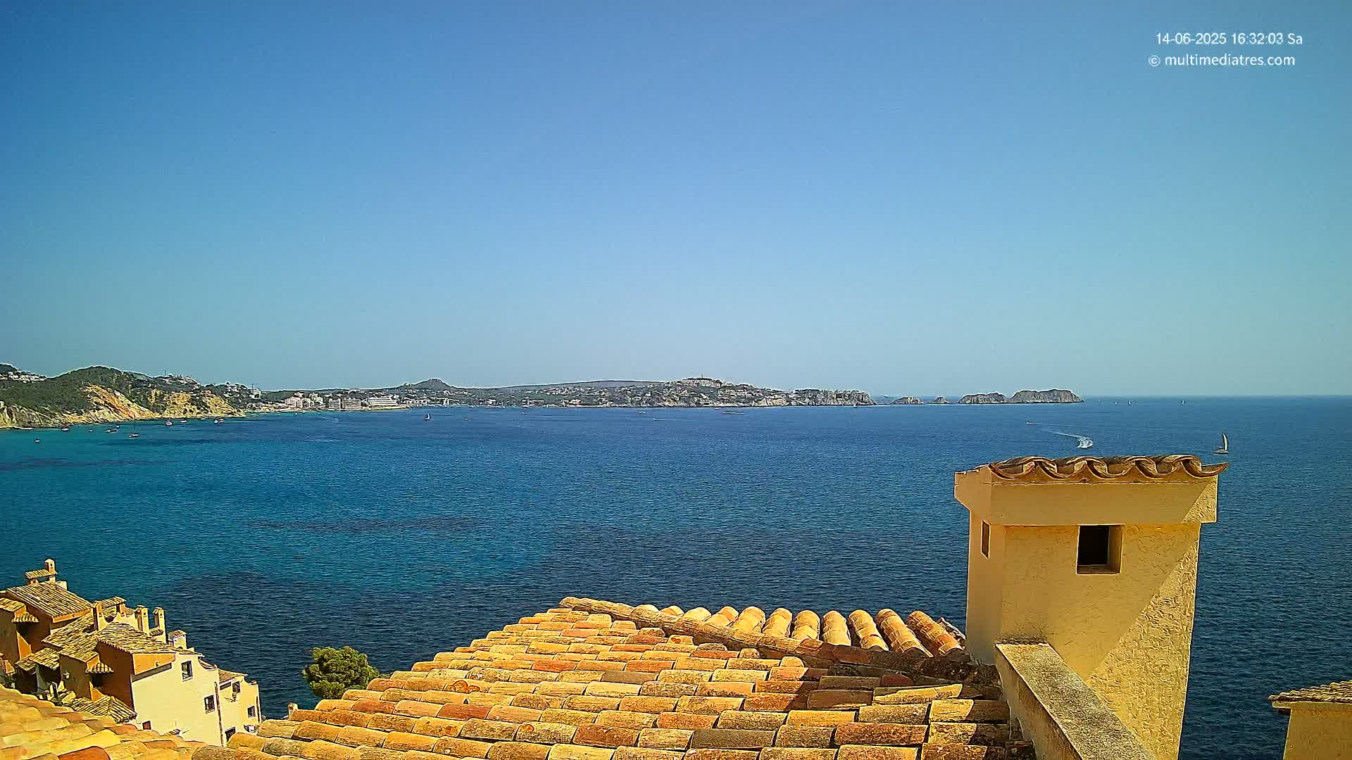 A terracotta roof overlooks a calm, blue ocean with a distant coastline under a clear blue sky.