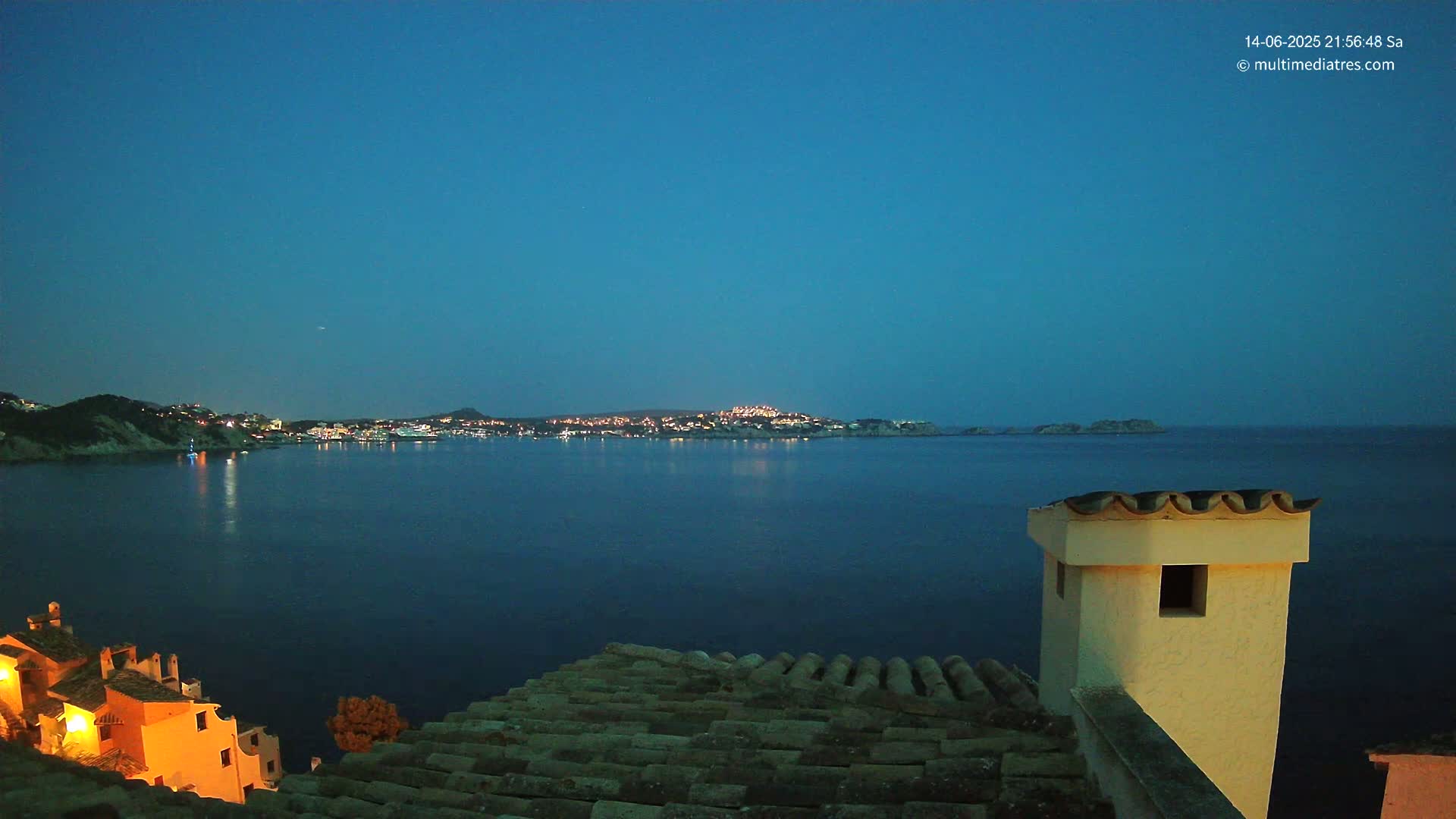 A terracotta roof overlooks a calm, blue ocean with a distant coastline under a clear blue sky.