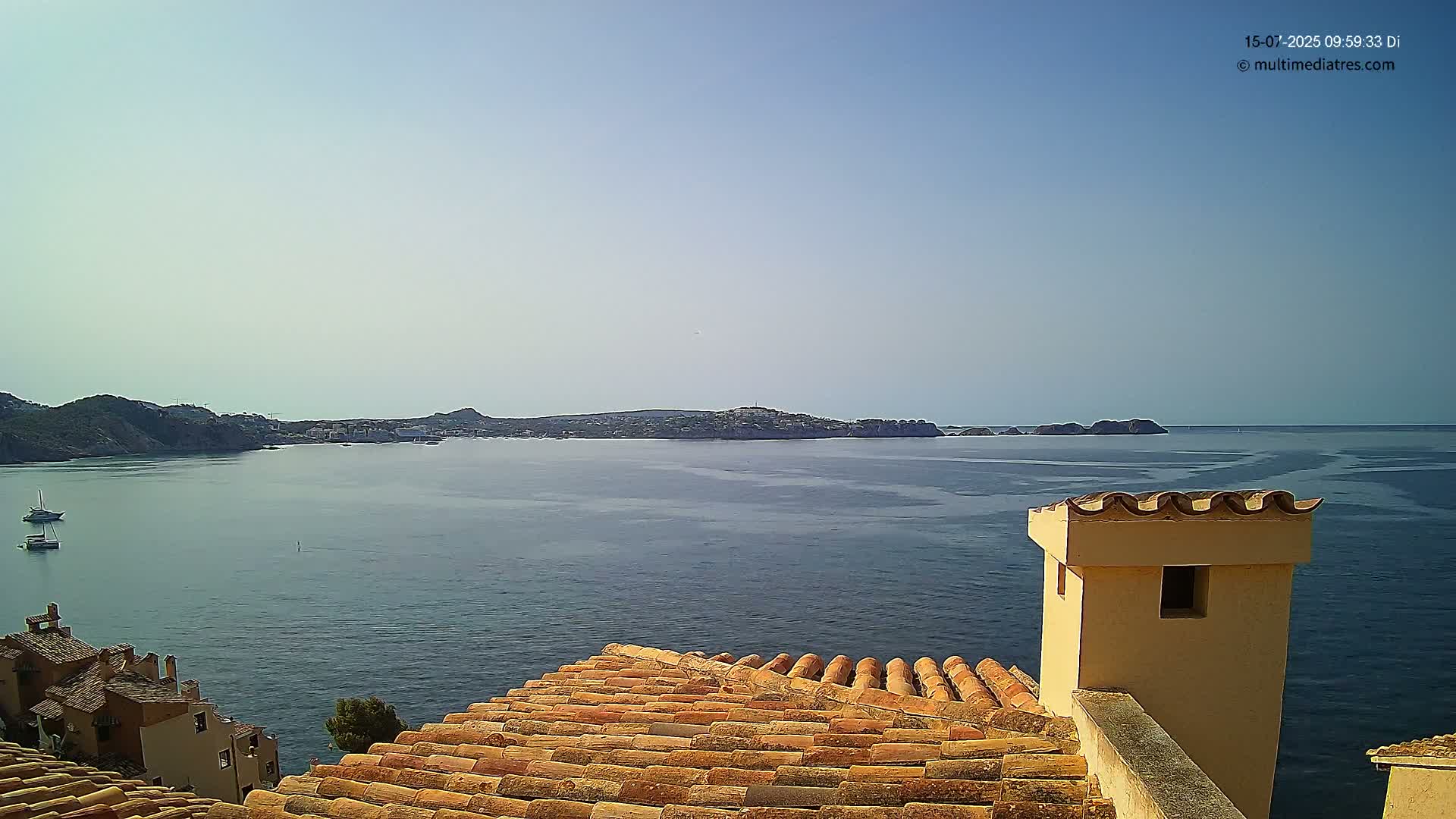 A clear, sunny day overlooks a calm body of water with a distant coastline and a few boats, viewed from a terracotta roof with a light-yellow chimney.