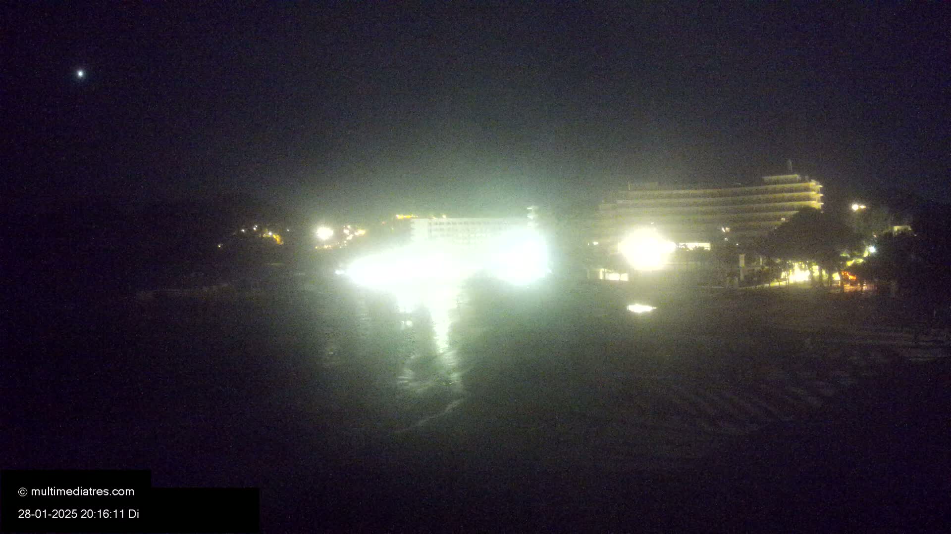 A brightly lit hotel is seen at night in foggy or hazy conditions, with a single bright star visible in the dark sky.
