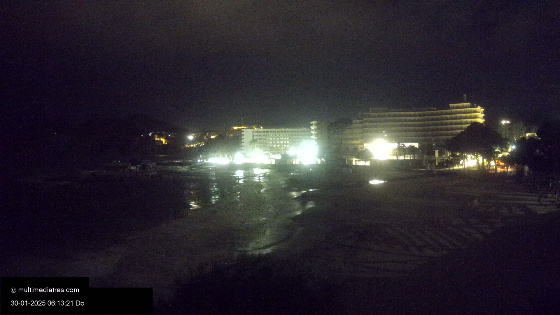 At night, illuminated hotels are situated near a dark beach under a clear sky.