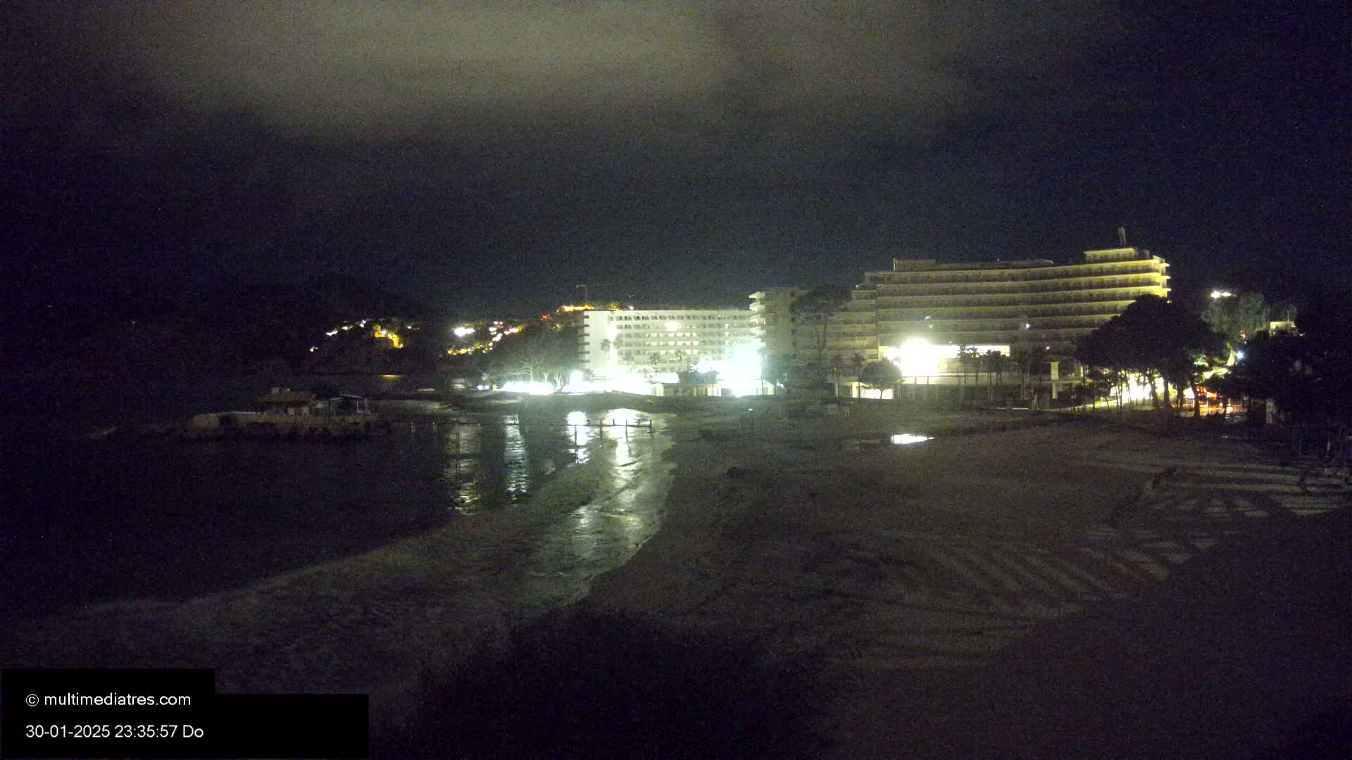 A nighttime view of a beach with two illuminated hotels and a calm body of water.