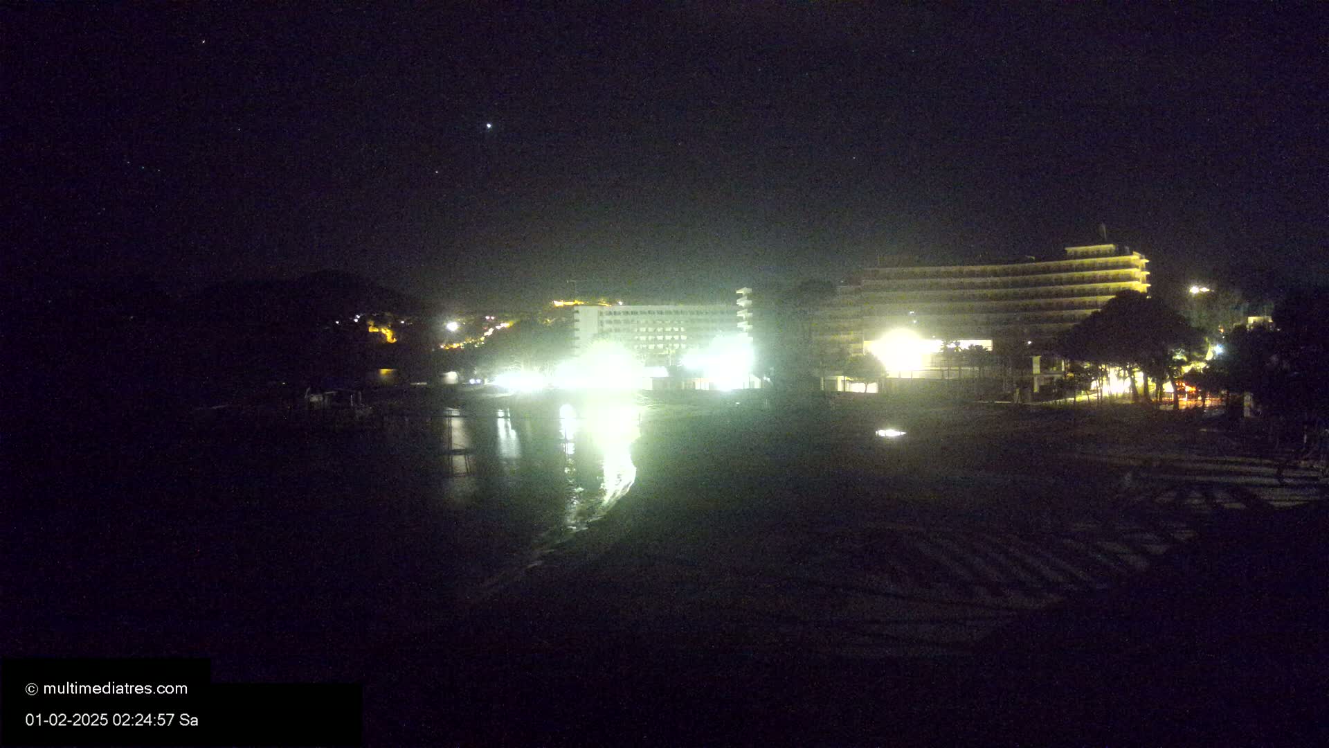 A nighttime view of brightly lit hotels and a beach, under a clear, starry sky.