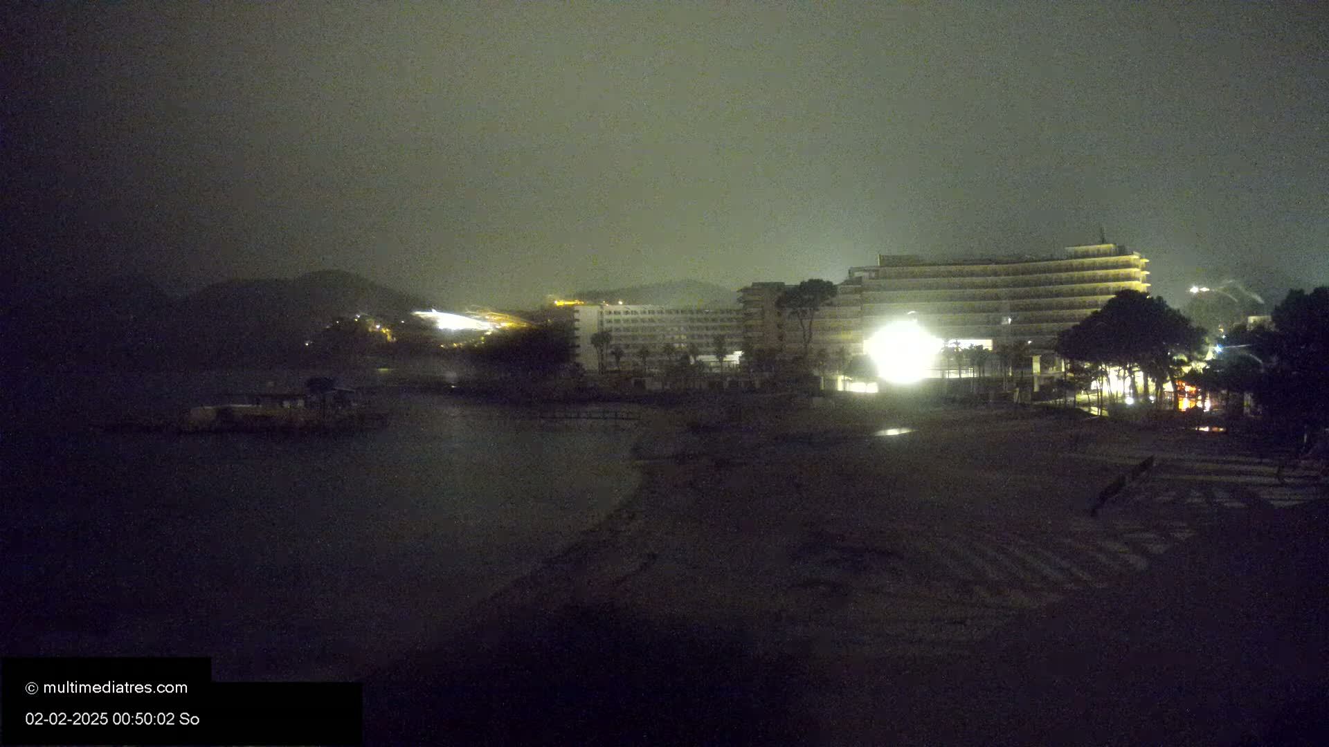 A nighttime view of a beach with a large hotel in the background under foggy conditions.