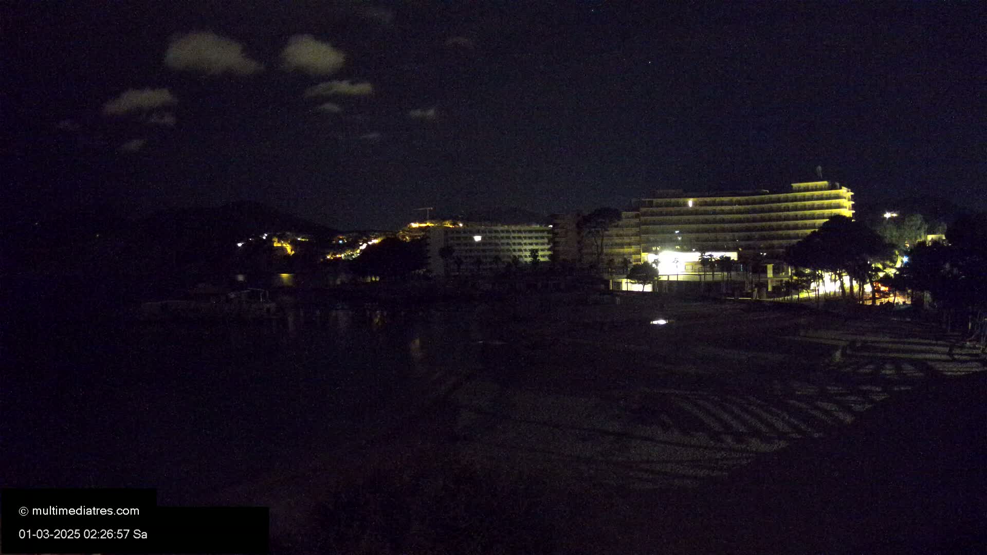 A nighttime view of a brightly lit hotel on a dark beach under a slightly cloudy sky.