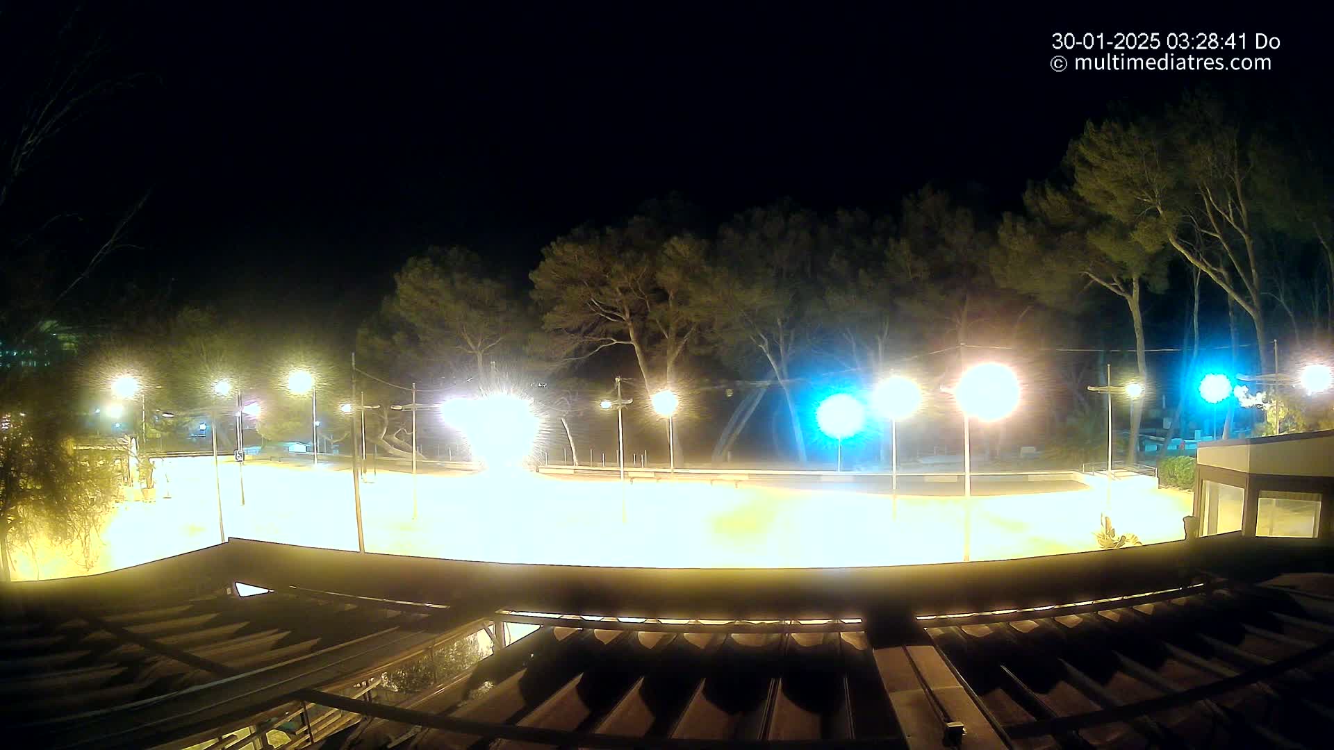 A brightly lit, empty outdoor area at night, surrounded by trees and illuminated by numerous lampposts.