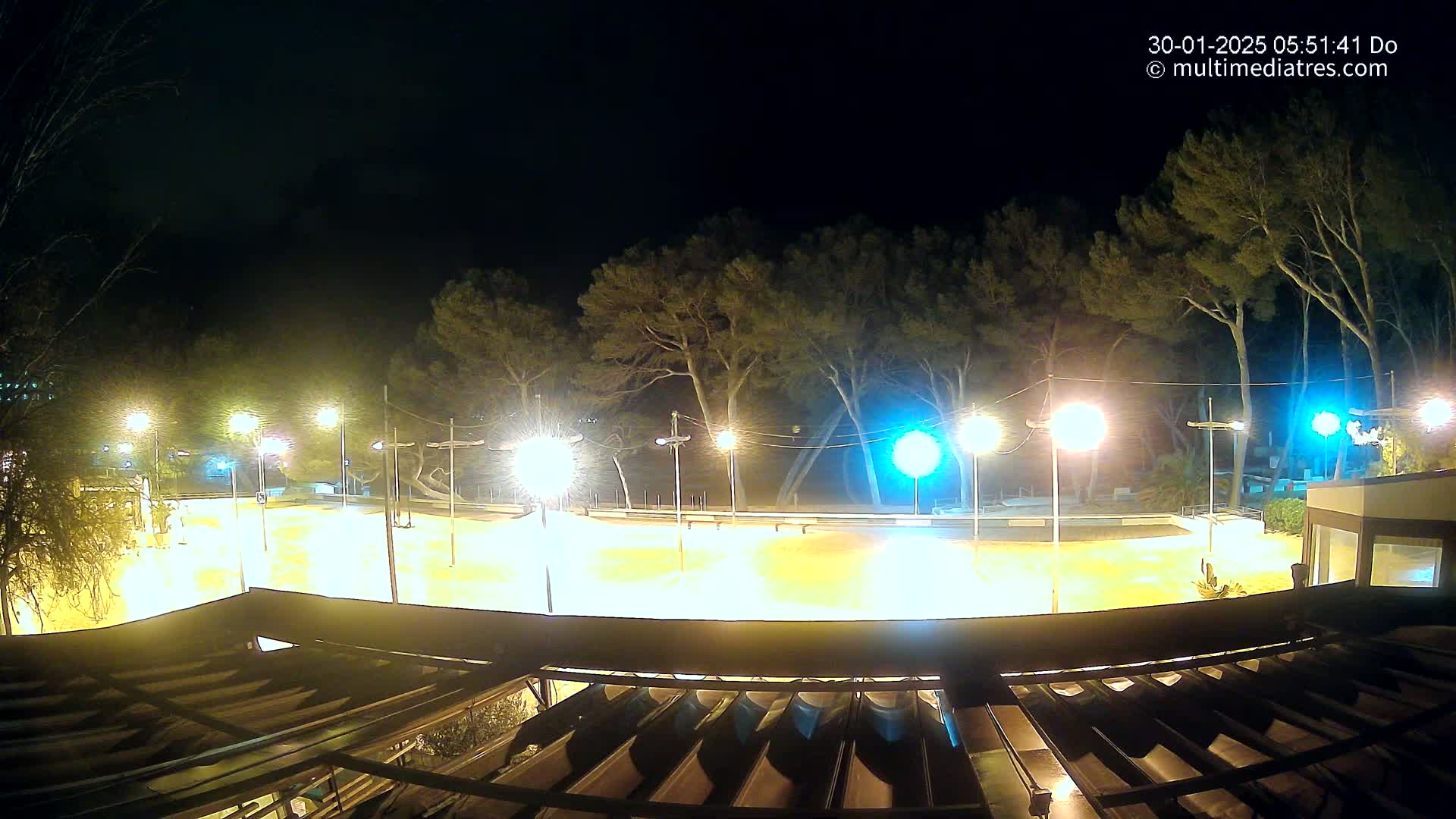 A brightly lit, empty plaza at night, surrounded by trees under a dark sky.