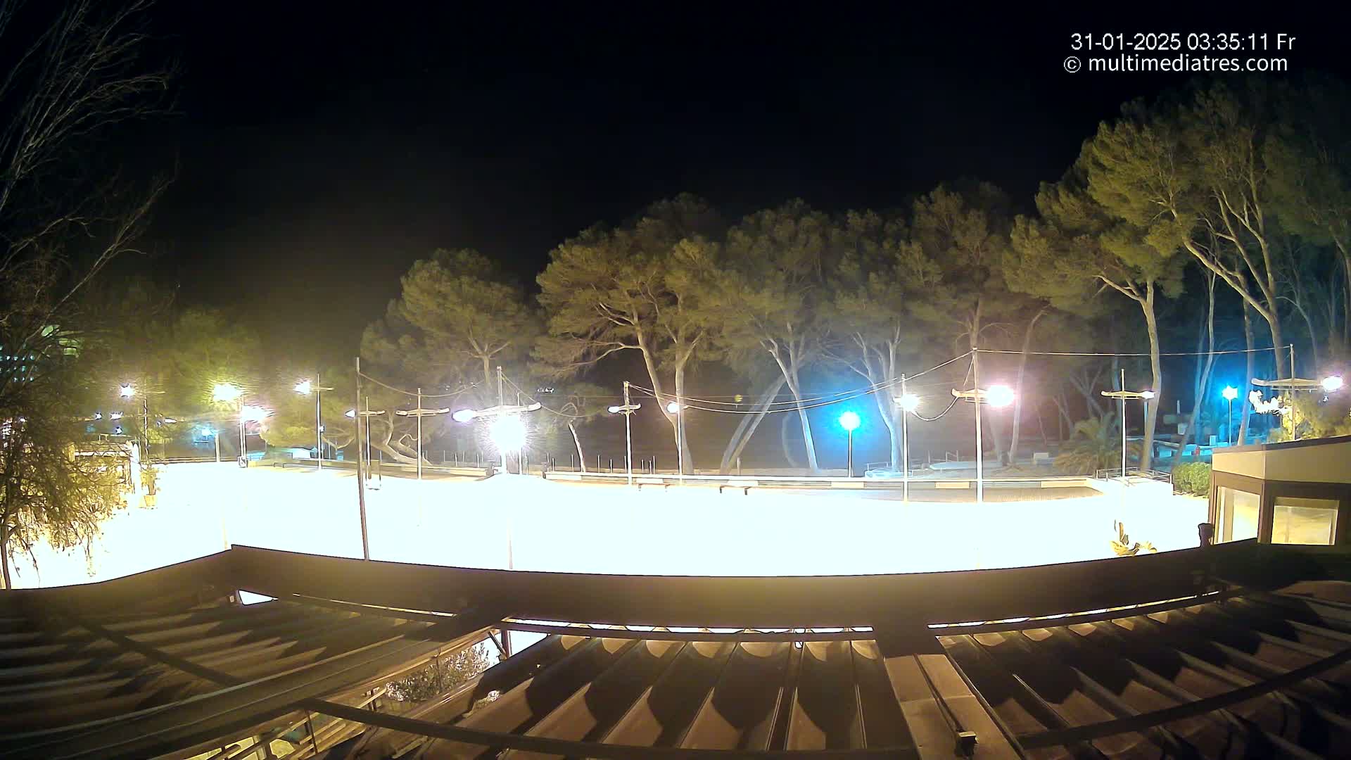 A brightly lit, empty paved area at night, surrounded by trees and illuminated by numerous streetlights.