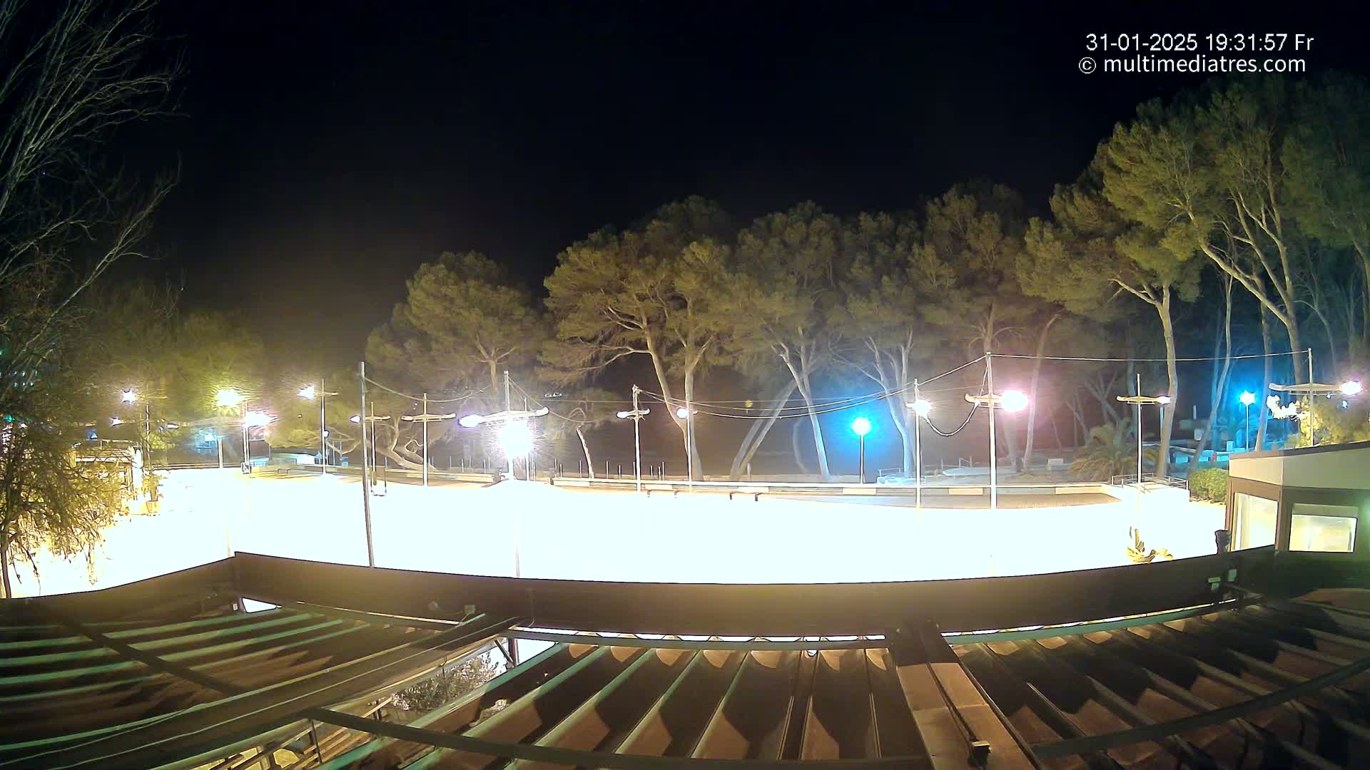 A brightly lit, empty plaza at night, surrounded by tall trees and illuminated by numerous streetlights.