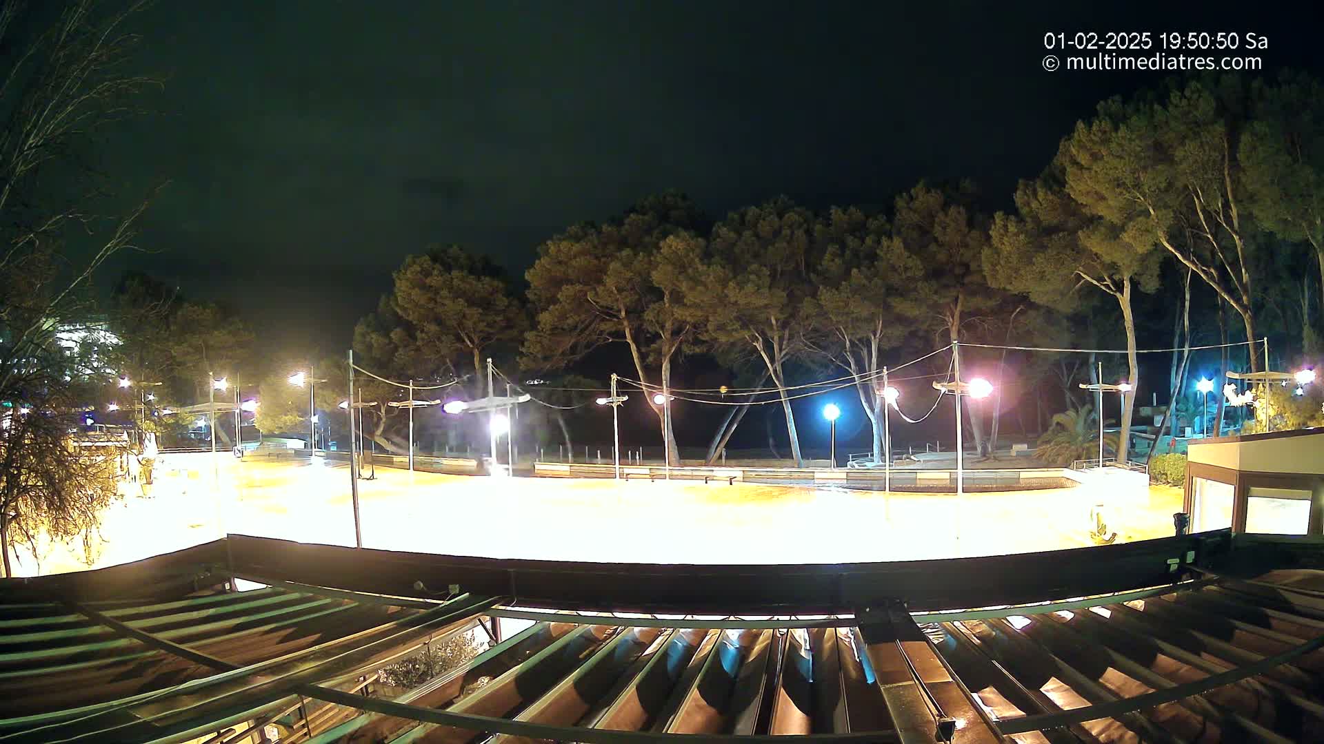A brightly lit outdoor rink or plaza at night, surrounded by trees under a dark sky.