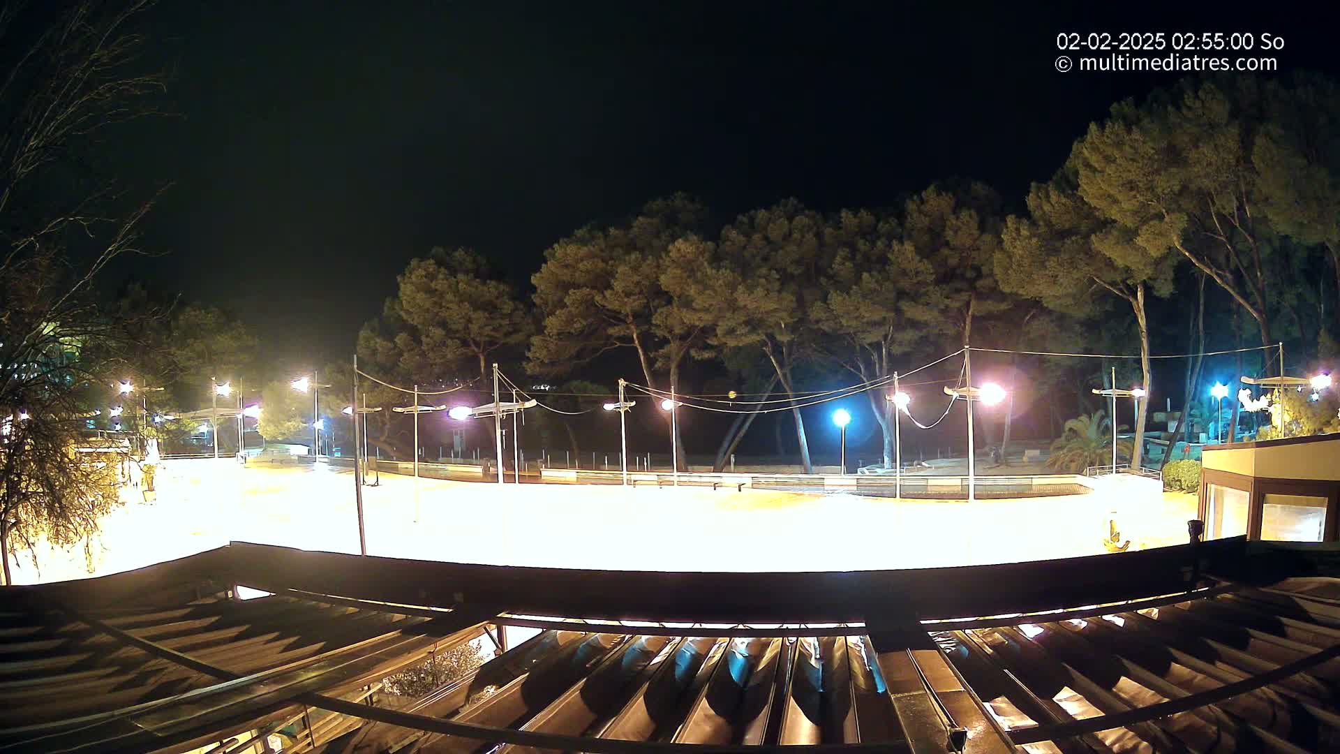 A brightly lit, empty outdoor rink is surrounded by trees at night.