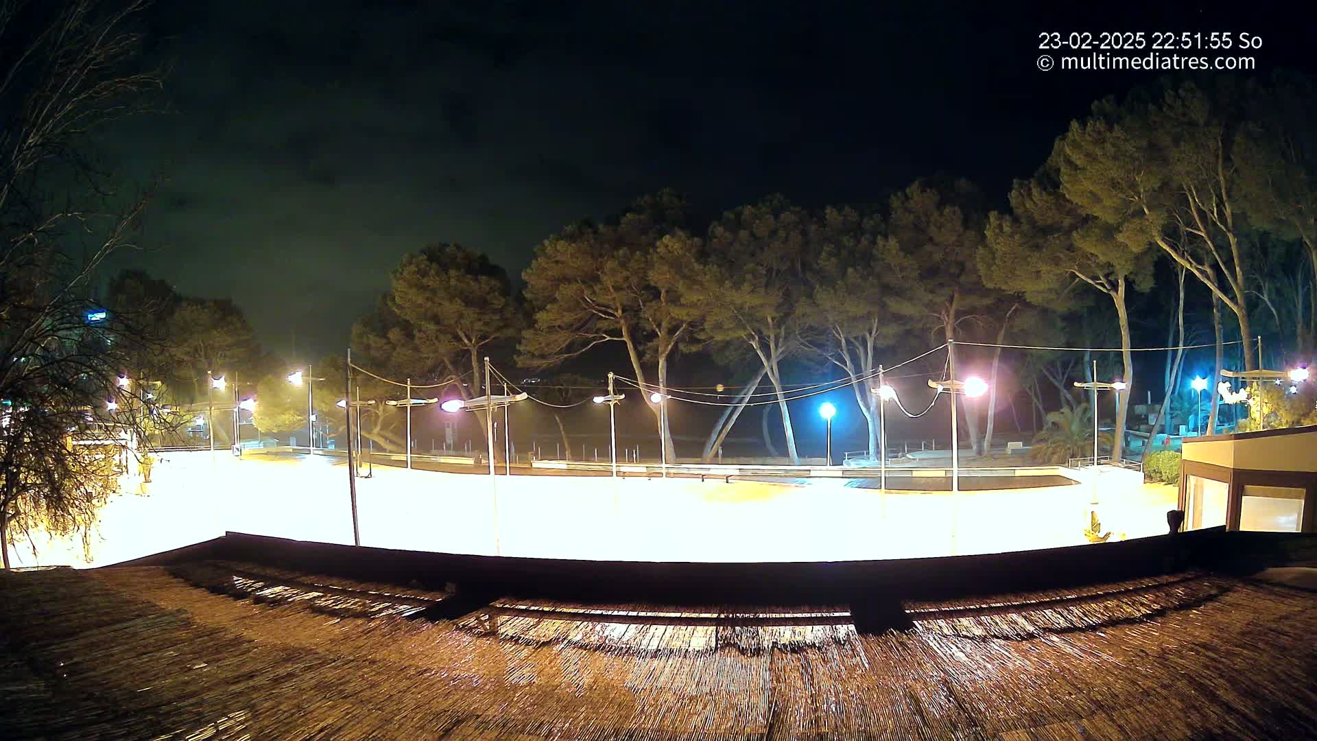 A brightly lit, empty plaza at night, surrounded by trees under a dark sky.