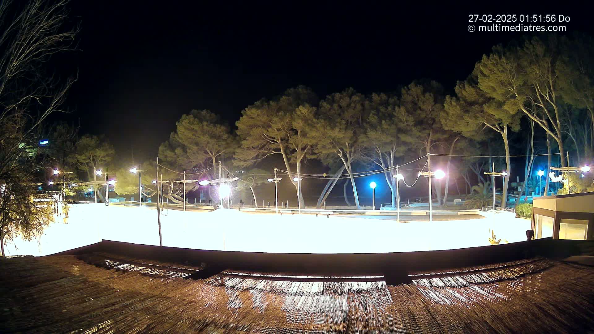 A brightly lit, empty plaza at night, surrounded by trees and illuminated by streetlights.