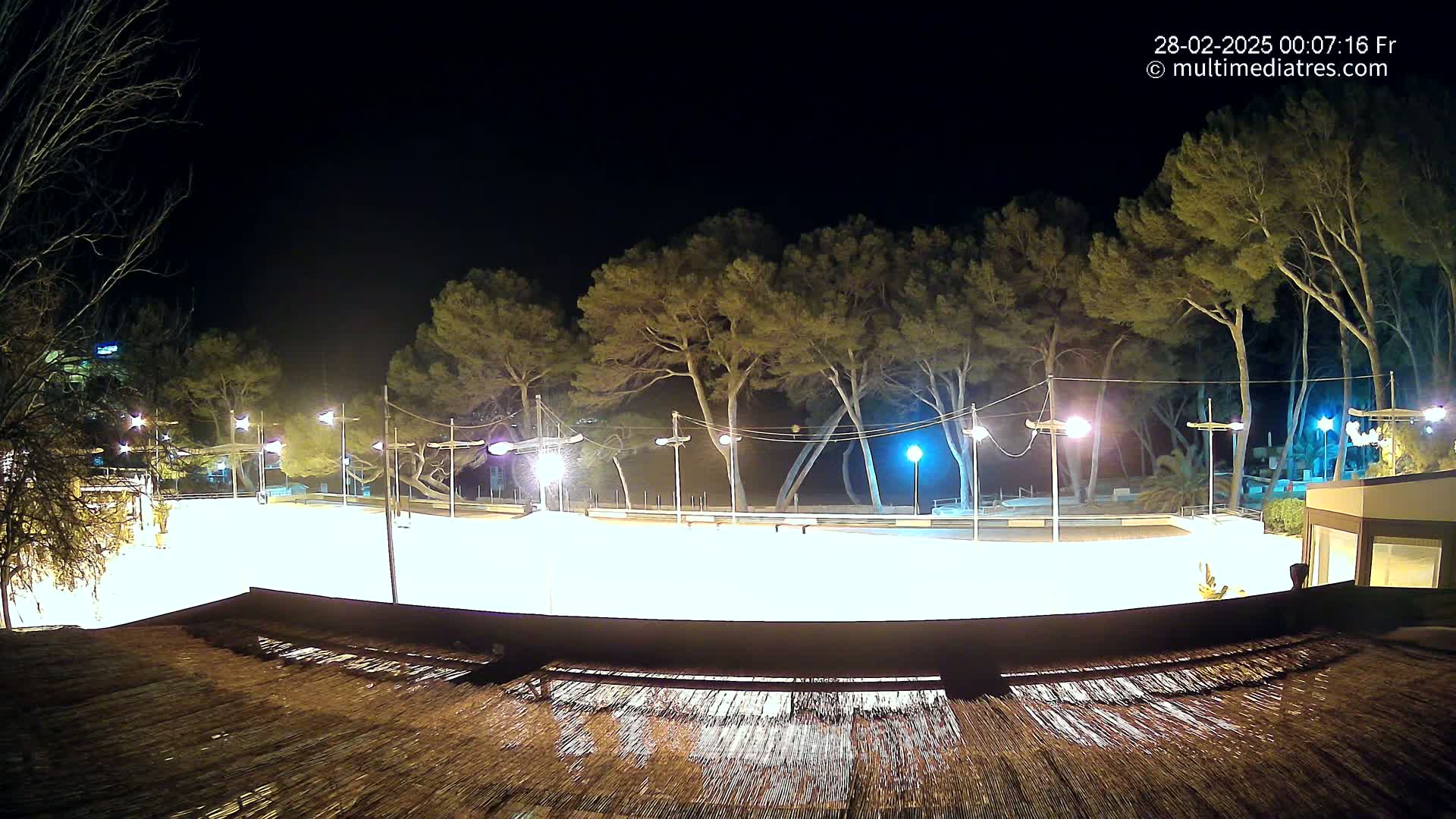 A brightly lit, empty outdoor rink at night, surrounded by trees and illuminated by numerous lights.